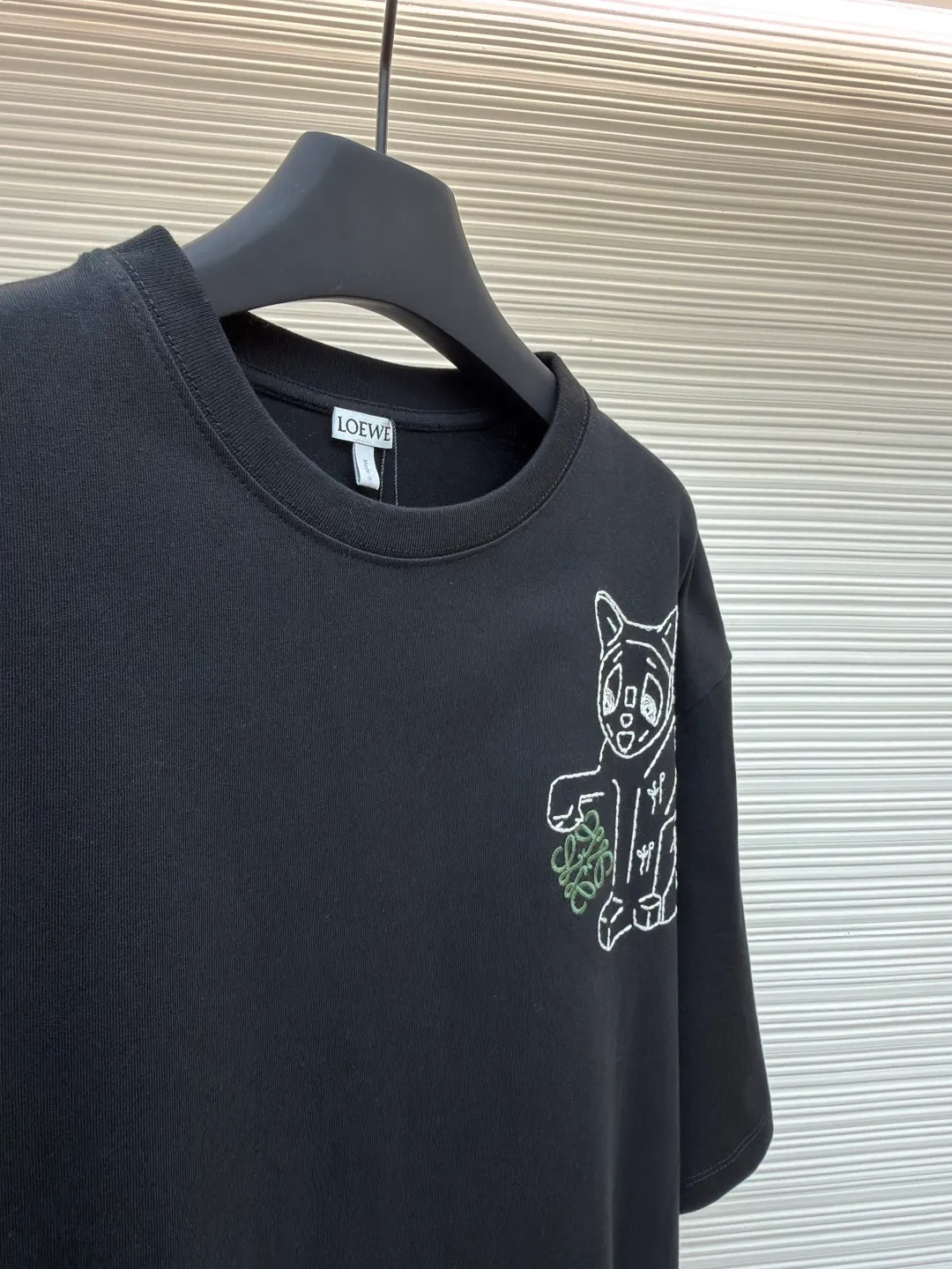 Loewe Cat Line Pattern Round Neck Short Sleeve ●Original version: Purchased and developed at 4330 ●Item number: 1681867-A00 ●Material: combed cotton fabric ●Technology: embroidery production ●Color: black ●Version: fitted version ●Weight: about 295 grams ●Size: XS-S-M-L ●Description: Made of 15S fine cotton plain fabric, 230g; with 32S double yarn thread, 300g. Plain weave fabric made from combed cotton fibers has a more orderly arrangement and higher density than ordinary cotton, so it has better texture and luster. 15S fine cotton plain fabric is a high-quality cotton fabric with the characteristics of softness, comfort, good breathability, and good durability. Anagram Embroidery Lucky Cat: The rice grain line embroidery process uses special ultra-fine embroidery thread and high-density stitching to create a pattern outline as delicate and continuous as grains. Its core feature lies in the precise arrangement of ultra-fine stitches, which require 12-15 stitches per centimeter to form full lines, and the edges present a handmade micro-waving effect. The fabric achieves a stroke-like gradient of thickness and flow. The overall pattern is light, breathable and smooth to the touch. It looks like a line outline from a distance, but the texture of interwoven fibers can be seen up close. It is especially suitable for expressing delicate details such as logo outlines and geometric borders. Anagram embroidery: Using three-dimensional embroidery technology, the logo clearly restores the spacing curve. The mercerized embroidery thread with luster is selected, combined with complex embroidery needlework and fine detail processing to create a three-dimensional relief embroidery effect. Classic trademark letter design, fine embroidery and dense stitching, clear font and strong sense of lines and three-dimensionality. The overall wiring is straight and delicate, the fabric is comfortable and soft, and the color is consistent without color difference. It can be matched with the same style to create a fashionable look and control various occasions. Customized accessories, complete with three standards, same style for men and women!