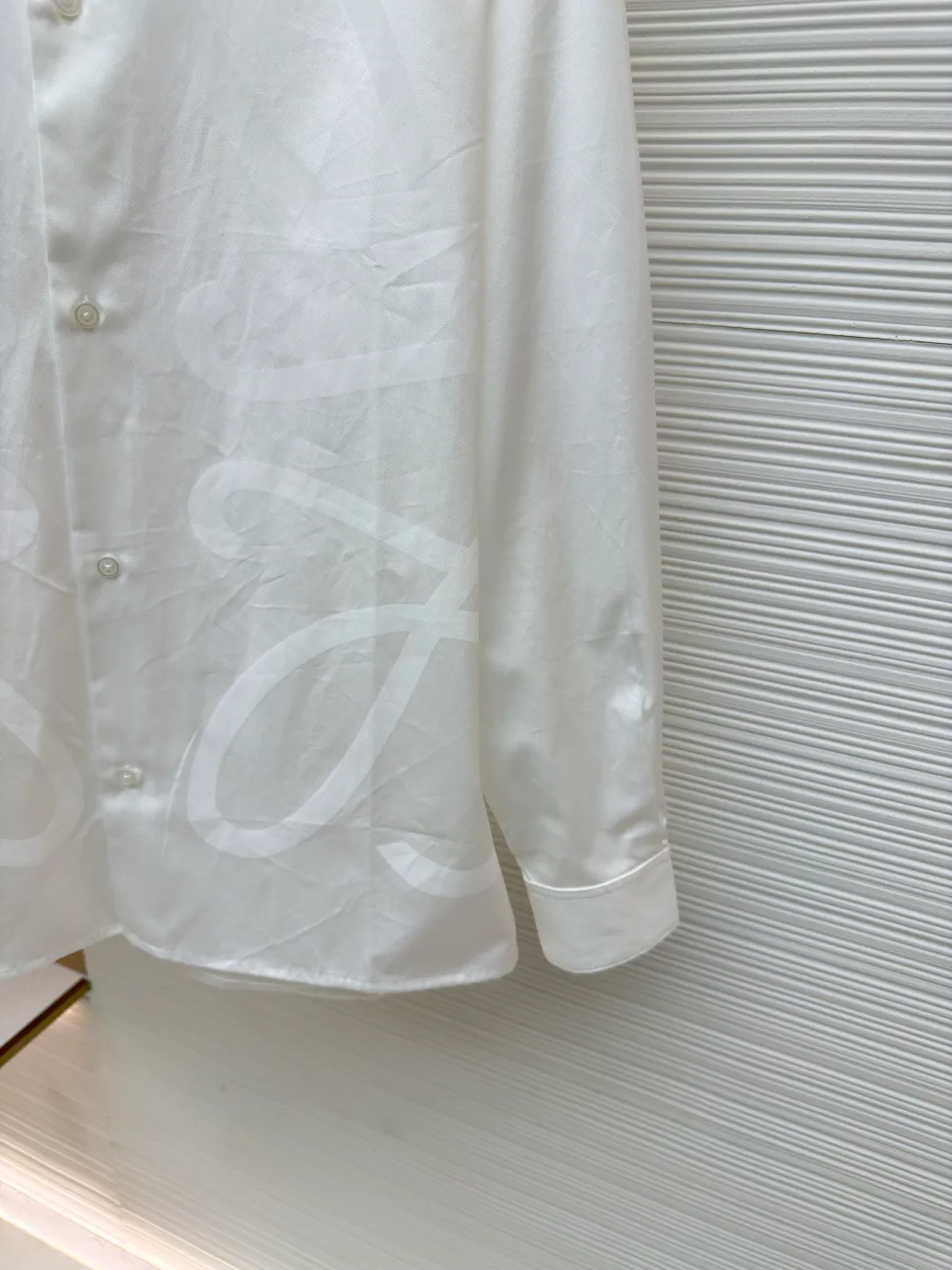 Loewe concealed logo lapel shirt ●Original version: Purchased and developed by 5268 ●Item No.: 1680722-A75 ●Fabric: Light cotton poplin shirt fabric ●Technology: Printing ●Version: Fitted version ●Weight: about 270 grams ●Size: 36-38-40-42 ●Description: Poplin is a classic cotton fabric characterized by a large density difference between warp and weft yarns, forming a fine diamond-shaped grainy texture. This structure not only gives the fabric a refreshing and breathable wearing feel, but also ensures that its texture is light and thin but has a crisp texture, avoiding the shortcomings of ordinary thin cotton that easily collapses, perfectly supporting the neat silhouette of the shirt, while maintaining the unique skin-friendly comfort of cotton. The chest is decorated with a discharge printing process; discharge printing is a special process that erodes through the dyed base fabric to reveal the light-colored pattern of the original fabric. This makes the Anagram logo not simply covered on the fabric, but integrated with the fabric, feeling smooth and traceless, showing a low-key and high-end matte effect. Fit and design The shirt adopts a loose fit of standard length; it is precisely tailored to the pattern. It is neither too loose nor deliberately slim, aiming to create a clean silhouette and is extremely tolerant to all body types. The standard length ensures that the hem can be tucked into trousers or hang naturally, meeting a variety of wear needs, including formal and casual. The overall wiring is straight and delicate, the fabric is comfortable and soft, and the color is consistent without color difference. It can be matched with the same style to create a fashionable look and control various occasions. Customized accessories, complete with three standards, same style for men and women!