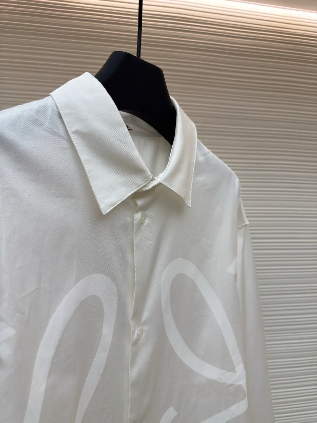 Loewe concealed logo lapel shirt ●Original version: Purchased and developed by 5268 ●Item No.: 1680722-A75 ●Fabric: Light cotton poplin shirt fabric ●Technology: Printing ●Version: Fitted version ●Weight: about 270 grams ●Size: 36-38-40-42 ●Description: Poplin is a classic cotton fabric characterized by a large density difference between warp and weft yarns, forming a fine diamond-shaped grainy texture. This structure not only gives the fabric a refreshing and breathable wearing feel, but also ensures that its texture is light and thin but has a crisp texture, avoiding the shortcomings of ordinary thin cotton that easily collapses, perfectly supporting the neat silhouette of the shirt, while maintaining the unique skin-friendly comfort of cotton. The chest is decorated with a discharge printing process; discharge printing is a special process that erodes through the dyed base fabric to reveal the light-colored pattern of the original fabric. This makes the Anagram logo not simply covered on the fabric, but integrated with the fabric, feeling smooth and traceless, showing a low-key and high-end matte effect. Fit and design The shirt adopts a loose fit of standard length; it is precisely tailored to the pattern. It is neither too loose nor deliberately slim, aiming to create a clean silhouette and is extremely tolerant to all body types. The standard length ensures that the hem can be tucked into trousers or hang naturally, meeting a variety of wear needs, including formal and casual. The overall wiring is straight and delicate, the fabric is comfortable and soft, and the color is consistent without color difference. It can be matched with the same style to create a fashionable look and control various occasions. Customized accessories, complete with three standards, same style for men and women!