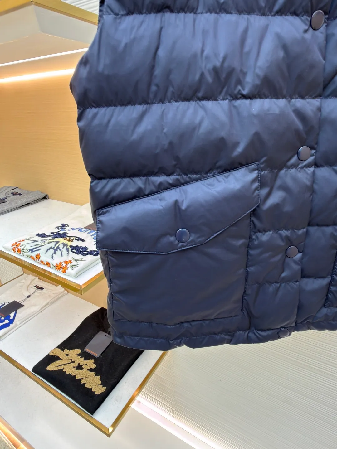 MIUMIU rib down lapel vest ●Original version: Purchased and developed for 12999 ●Item number: 1681785-C05 ●Fabric: goose down fabric ●Technology: mechanical down filling ●Color: navy blue ●Version: fitted version ●Weight: about 350 grams ●Size: 36-38-40-42 ●Description: Down anti-drilling liner is a kind of inner liner specially used for down jackets. It is usually made of high-density, anti-drilling down and good breathability materials. It can effectively prevent down from drilling out while maintaining the warmth and breathability of down jackets. Goose down filling is a high-quality filling in down jackets. It is rich in down, and because goose down has a higher loft, it can lock in more air, making the down jacket warmer. Down is soft and delicate. It feels soft and comfortable when worn on the human body, without the foreign body feeling caused by other fillings. After aurora printing, the pattern containing special additives is heat-pressed and transferred to the fabric in the form of a film, and the process parameters are adjusted to give it a slightly aged texture. This not only achieves the decorative purpose of the brand logo, but also avoids the stiffness often found in new technology fabrics because of its retro treatment of details. The design of the shirt collar allows the vest to increase its versatility. The snap closure provides a faster, smoother and more even force-on and take-off experience, especially when worn as an inner layer, making it less likely to snag with outer clothing. The elastic drawstring hem can be tightened by the drawstring, effectively preventing cold air from pouring in from the bottom and locking in body heat. The flap pocket is a classic outdoor functional design that prevents rain, wind and snow from entering the pocket, and is equipped with buttons for a more durable and quieter closure.