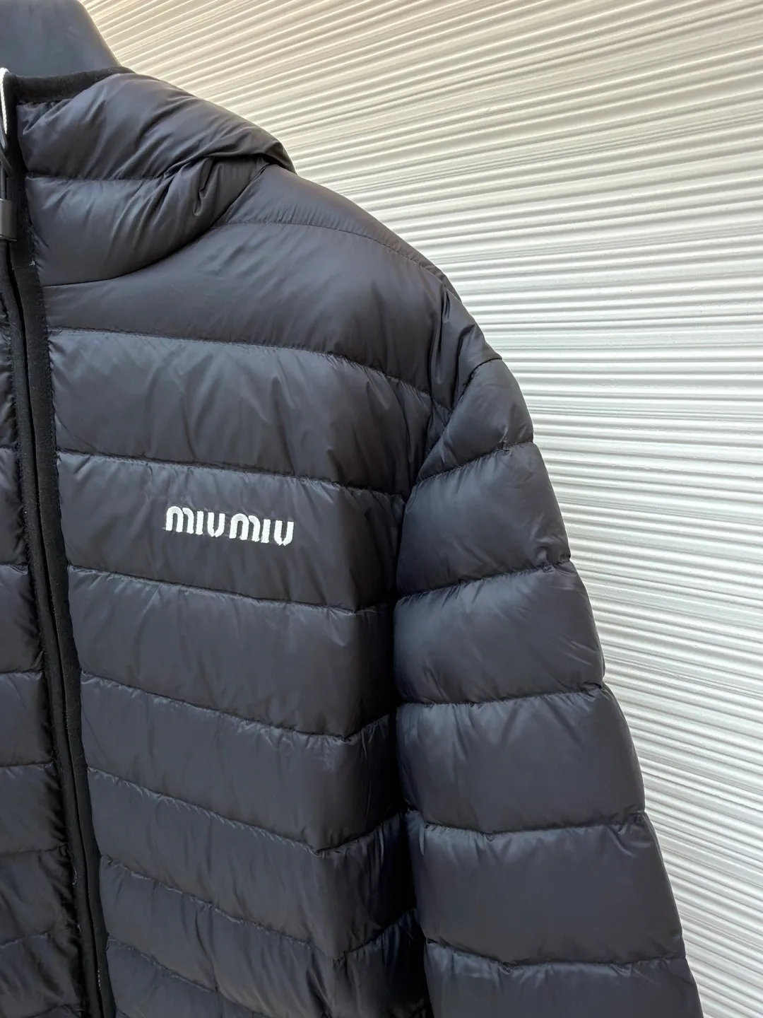 MIU MIU hooded down jacket ●Item number: 1681314-C55 ●Material: white duck down fabric ●Technology: mechanical down filling ●Color: black ●Version: fitted version ●Weight: about 615 grams ●Size: S-M-L-XL ●Description: This is a light down jacket from the MiuMiu brand. Its craftsmanship details are as follows: It is made of exquisite pongé fabric made of 100% recycled polyester fiber. This fabric has good windproof performance, and at the same time has a delicate texture and a high-end luster. It has high fluffiness, excellent warmth retention and is very light overall, allowing the wearer to gain warmth without any heavy burden. It has a three-dimensional cut and a neat silhouette. Precision stitching technology is used during sewing to form regular quilting lines, which not only serves to fix the down, but also enhances the structure and design of the garment. The stitches are fine and even, and the seams are smooth, reflecting the exquisite craftsmanship of garment making. Equipped with a customized wax zipper, the zipper is smooth and durable, and the zipper puller has brand details and a high-quality feel. The hooded design fits the head and increases warmth; the drawstring cuffs can be adjusted according to needs to prevent cold wind from entering; the elastic drawstring at the hem can adjust the looseness of the hem, improving the comfort and practicality of wearing; there is the brand's embroidered logo on the chest, with fine craftsmanship and highlighting the brand identity.