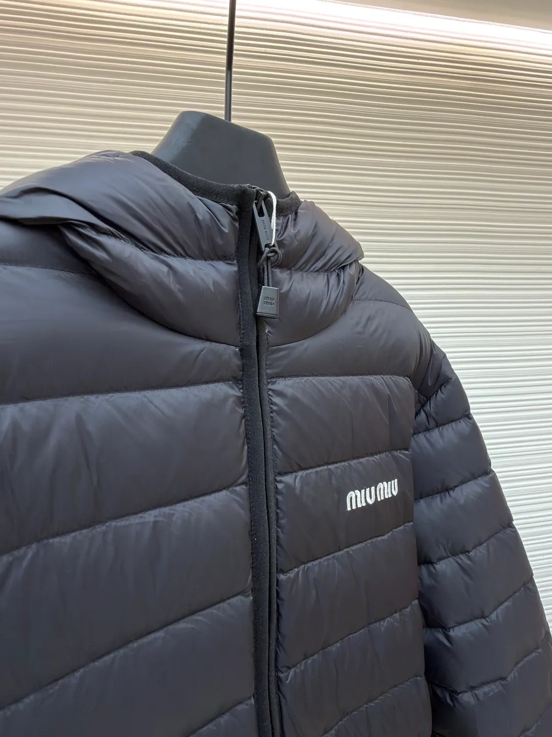 MIU MIU hooded down jacket ●Item number: 1681314-C55 ●Material: white duck down fabric ●Technology: mechanical down filling ●Color: black ●Version: fitted version ●Weight: about 615 grams ●Size: S-M-L-XL ●Description: This is a light down jacket from the MiuMiu brand. Its craftsmanship details are as follows: It is made of exquisite pongé fabric made of 100% recycled polyester fiber. This fabric has good windproof performance, and at the same time has a delicate texture and a high-end luster. It has high fluffiness, excellent warmth retention and is very light overall, allowing the wearer to gain warmth without any heavy burden. It has a three-dimensional cut and a neat silhouette. Precision stitching technology is used during sewing to form regular quilting lines, which not only serves to fix the down, but also enhances the structure and design of the garment. The stitches are fine and even, and the seams are smooth, reflecting the exquisite craftsmanship of garment making. Equipped with a customized wax zipper, the zipper is smooth and durable, and the zipper puller has brand details and a high-quality feel. The hooded design fits the head and increases warmth; the drawstring cuffs can be adjusted according to needs to prevent cold wind from entering; the elastic drawstring at the hem can adjust the looseness of the hem, improving the comfort and practicality of wearing; there is the brand's embroidered logo on the chest, with fine craftsmanship and highlighting the brand identity.