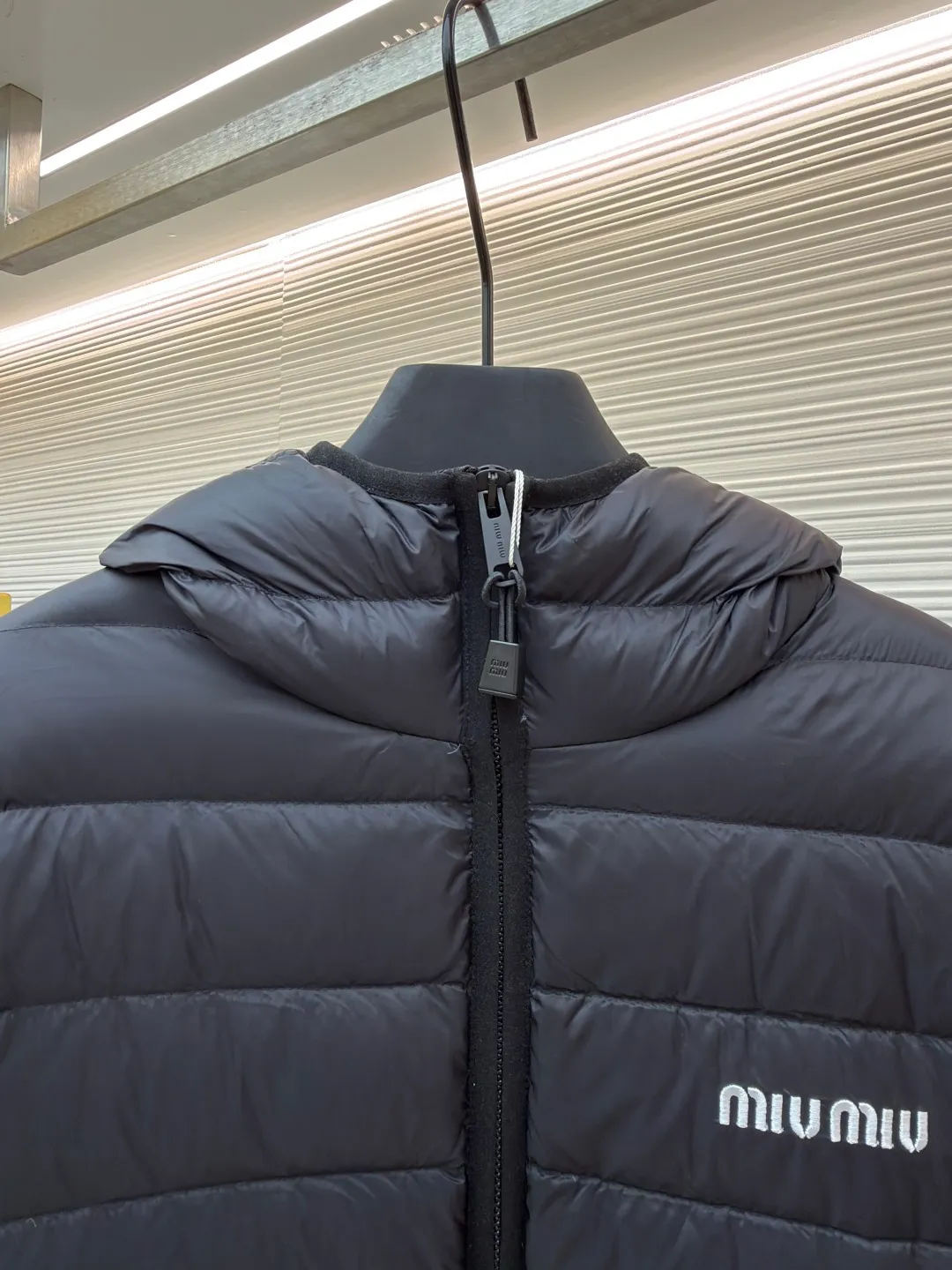 MIU MIU hooded down jacket ●Item number: 1681314-C55 ●Material: white duck down fabric ●Technology: mechanical down filling ●Color: black ●Version: fitted version ●Weight: about 615 grams ●Size: S-M-L-XL ●Description: This is a light down jacket from the MiuMiu brand. Its craftsmanship details are as follows: It is made of exquisite pongé fabric made of 100% recycled polyester fiber. This fabric has good windproof performance, and at the same time has a delicate texture and a high-end luster. It has high fluffiness, excellent warmth retention and is very light overall, allowing the wearer to gain warmth without any heavy burden. It has a three-dimensional cut and a neat silhouette. Precision stitching technology is used during sewing to form regular quilting lines, which not only serves to fix the down, but also enhances the structure and design of the garment. The stitches are fine and even, and the seams are smooth, reflecting the exquisite craftsmanship of garment making. Equipped with a customized wax zipper, the zipper is smooth and durable, and the zipper puller has brand details and a high-quality feel. The hooded design fits the head and increases warmth; the drawstring cuffs can be adjusted according to needs to prevent cold wind from entering; the elastic drawstring at the hem can adjust the looseness of the hem, improving the comfort and practicality of wearing; there is the brand's embroidered logo on the chest, with fine craftsmanship and highlighting the brand identity.