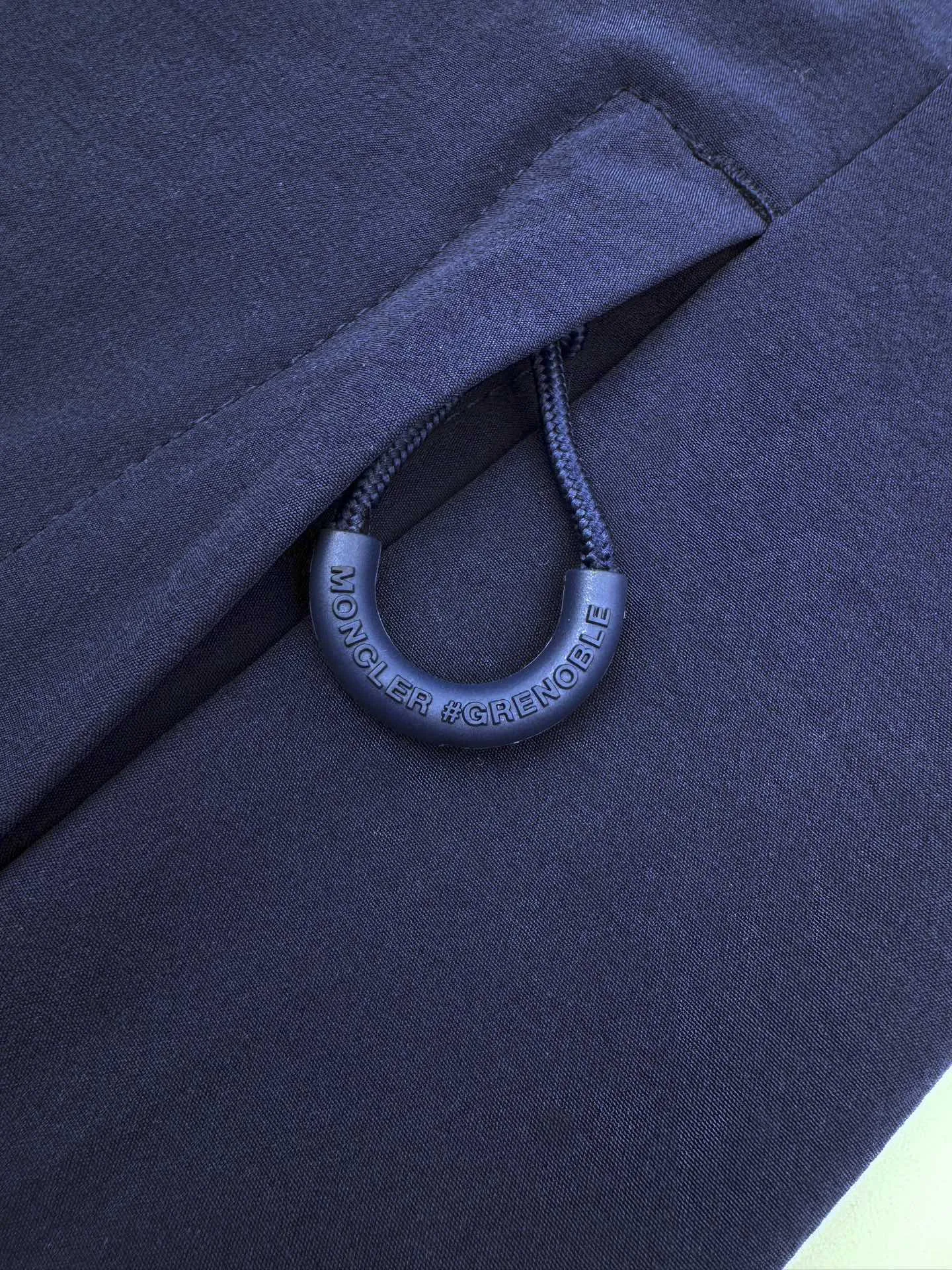 P610 Moncler Grenoble functional outdoor jacket Custom dyed double stretch mercerized poplin Custom dyed soft mesh pongee Excellent texture Comfortable and close to the skin Navy blue inspired by the deep sea Low-key statement of the contemporary gentleman Precision narrative of functional pocket system Balance of function and aesthetics The iconic Moncler logo appears on the sleeves for full recognition The triangular logo of the same color is hidden into the fabric texture like a mark in the undercurrent of the deep sea, extremely invisible and visible The detachable sleeve design allows for diversified outfits The style can be switched freely, chic and noble, taking into account the balance between outdoor practicality and urban aesthetics, leading the fashion. Process 1: Using three-in-one process, the glue is evenly coated on the surface of the substrate that needs to be composited, and then dried and solidified. Then the substrate coated with the adhesive film is laminated with the non-woven fabric, and then cooled and solidified, and then composited with the filter non-woven fabric. The workmanship is cumbersome and complex, time-consuming and labor-intensive. Process 2: Embossed composite technology through computer scanning. Ensure that the size and shape of the imprint are consistent with the original, then use special glue as an adhesive to combine and then solidify to achieve complete dryness and the best bonding effect. Process 3: Use CNC laser burning and cutting. Based on the high-energy characteristics of the laser, the moving path of the laser beam is precisely controlled by the laser generator to achieve precise cutting of the shape. Process 4: Template machine bag opening. The preset template guides the position, shape and size of the bag opening. The accuracy ensures the quality of the bag opening effect. Process 5: Uses infrared special machine to tack buttons. The position is more precise and firm. Accessories: Customized 1:1 Moncler snap button Customized 1:1 Moncler resin buckle Customized 1:1 Moncler logo stamp Customized 1:1 Moncler logo armband Customized 1:1 Moncler zipper rope ring Customized 1:1 Moncler zipper pull Customized 1:1 Moncler trademark Version: Loose version Function: Detachable sleeve splicing Style can be switched at will Size: 1 2 3 4
