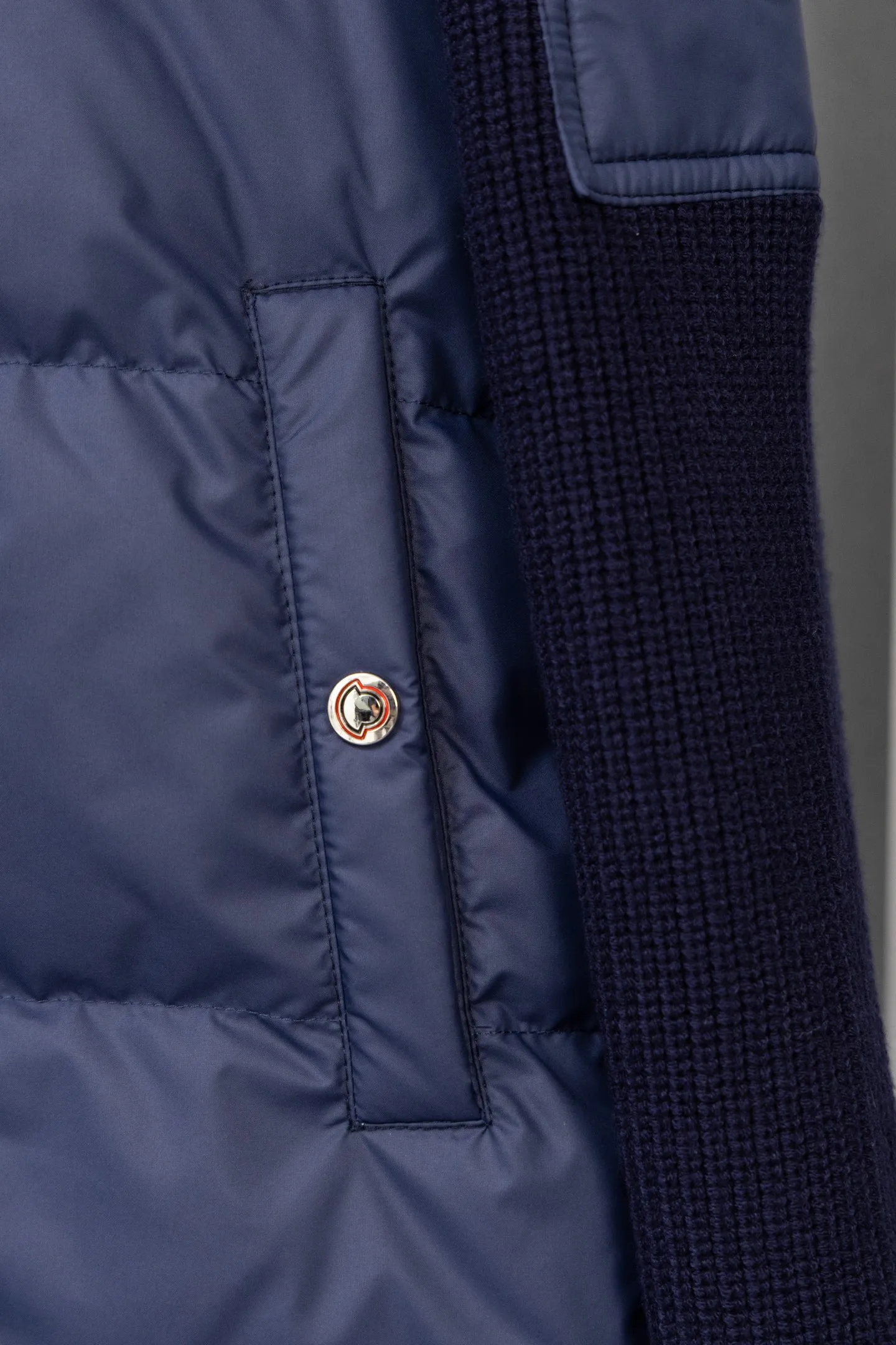 P560 Style number: M046 This is a knitted patchwork down jacket from Moncler. It combines the brand's high-end outdoor genes and fashion design. It is a luxurious item with both warmth and style in autumn and winter. Design highlights: Material splicing: Pure wool knitted sleeves are spliced ​​with a down front filled with 90 white duck down. The knitted part is soft and breathable, and the down part is fluffy and warm, achieving a dual fusion of style and function.  Detailed logo: The iconic Moncler badge pocket on the left arm is a classic embodiment of brand recognition; the stand-up collar design with a two-way zipper not only improves warmth, but also strengthens the neat styling.  Color embellishment: The contrasting red and blue stripes on the cuffs and hem inject vitality into the overall black tone, adding a retro college style charm. Craftsmanship and Quality: The down filling follows the European standard 90 down standard, with excellent fluffiness and down filling, with almost no stiff feeling. At the same time, it adopts the "line first and then separate down filling" process. The four-layer liner effectively prevents down from being drilled, and can maintain warmth even after long-term wear.  The knitted part is made of high-quality wool, which has a delicate touch and is not easily deformed. The splicing process with the down fabric is rigorous, showing a high-end texture level.  Style and Wearing This down jacket is based on the classic college style. The slim straight version can modify the body line and can be easily adapted to a variety of styles: it can be paired with jeans and casual shoes for a casual look on a daily basis. It can also be upgraded to an urban light luxury style by layering it with a turtleneck sweater inside and a suit outside. It is a key item in the winter wardrobe that is both practical and fashionable. Color: black, navy blue, sizes S-XL
