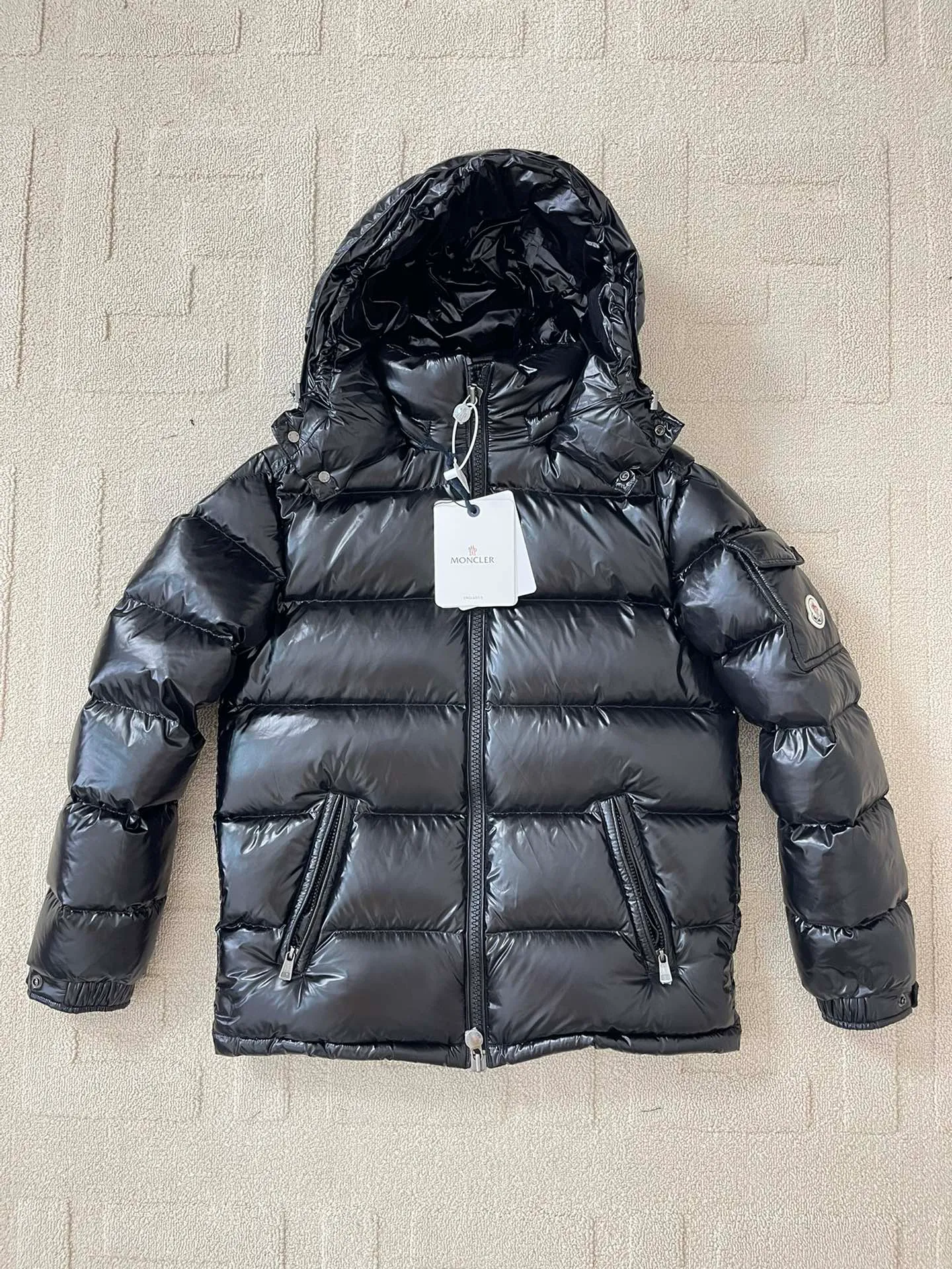 Flat detail P1180 Moncler Maya Men's Men's Short Down Jacket The Moncler Maya men's down jacket is made of shiny patented nylon with signature rectangular quilting, the epitome of Moncler style. A classic cropped design that transcends seasons and styles, it features a statement silhouette, removable hood and adjustable hem. The sleeves are embellished with classic patch pockets, showcasing the brand's signature style.  Fabric: 100% nylon, 90% white goose down Craftsmanship: Made of lacquered nylon, lacquered nylon lining filled with down, rectangular quilting, detachable hood with snaps that can be adjusted by drawstring, two-way zip fly, external and internal zippered pockets, adjustable elastic cuffs with snaps, hood with drawstring, sleeves with flap patch pockets, sleeves decorated with Moncler felt trademark.  Size: 123456 0548000