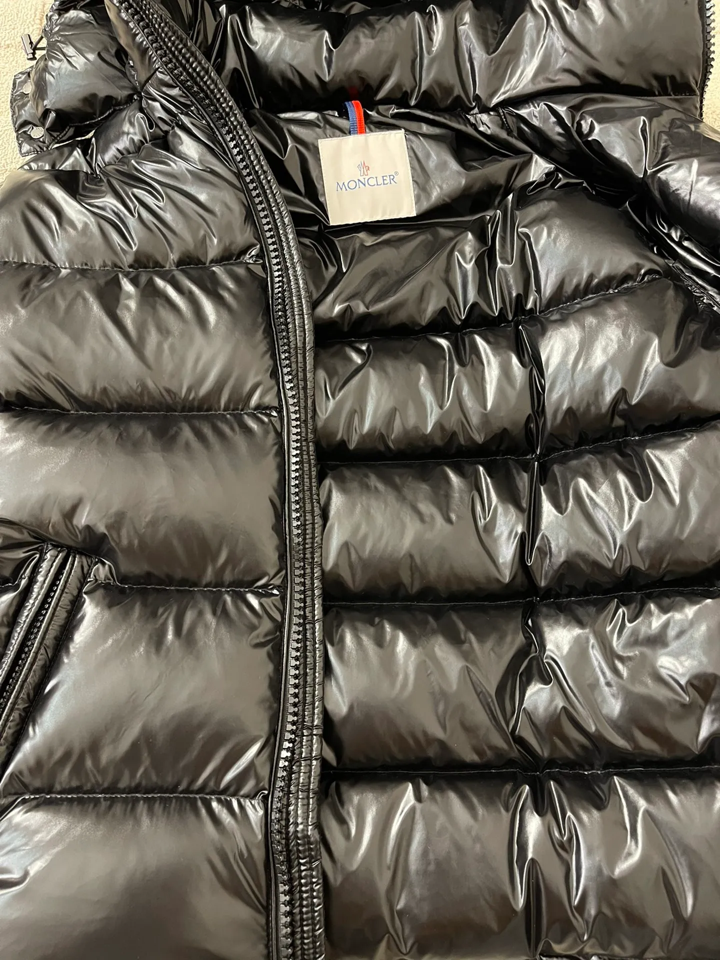 Flat detail P1180 Moncler Maya Men's Men's Short Down Jacket The Moncler Maya men's down jacket is made of shiny patented nylon with signature rectangular quilting, the epitome of Moncler style. A classic cropped design that transcends seasons and styles, it features a statement silhouette, removable hood and adjustable hem. The sleeves are embellished with classic patch pockets, showcasing the brand's signature style.  Fabric: 100% nylon, 90% white goose down Craftsmanship: Made of lacquered nylon, lacquered nylon lining filled with down, rectangular quilting, detachable hood with snaps that can be adjusted by drawstring, two-way zip fly, external and internal zippered pockets, adjustable elastic cuffs with snaps, hood with drawstring, sleeves with flap patch pockets, sleeves decorated with Moncler felt trademark.  Size: 123456 0548000