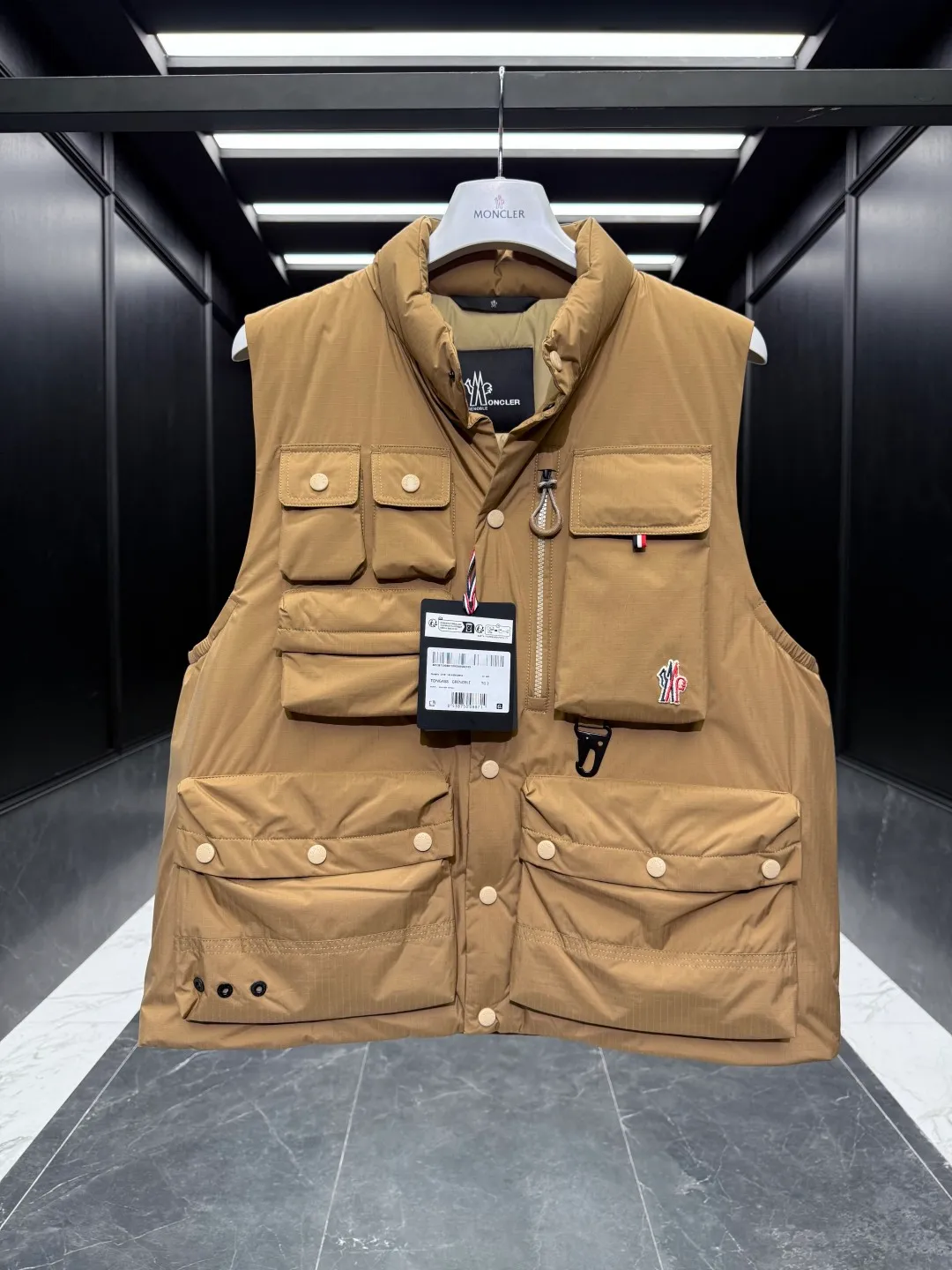 P820 ​​Premium Down ⬆️Moncler Grenoble Tongass Down Outdoor Vest. High-end Black Label Series. Original replacement fabric. Premium duck neck down filling. The Tongass Down Vest provides protection without being heavy and is specially designed for outdoor activities in mild weather.  The Tongass down vest is the result of research into lightweight performance outerwear. Functional fabric is tight and durable without adding extra weight. Features a large utility pocket and carabiner clip to reduce the amount of luggage you carry. Details •Designed for outdoor activities •Made from tight fabric •Polyester lining •Down filling •Snap button closure •Utility pockets with snap, zip and Velcro closure •Drawstring hem •Front carabiner •Reflective details Size: 1-5 Light Brown/Black D00780