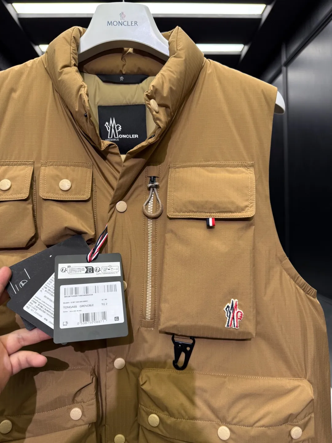 P860 Premium Down⬆️Moncler Grenoble Tongass Down Outdoor Vest. High-end Black Label Series. Original replacement fabric. Premium gooseneck filling. 🎁 Comes standard with a full set of counter gift box packaging. Upgraded original magnetic gift box. The Tongass Down Vest provides protection without being heavy, and is specially designed for outdoor activities in mild weather.  The Tongass down vest is the result of research into lightweight performance outerwear. Functional fabric is tight and durable without adding extra weight. Features a large utility pocket and carabiner clip to reduce the amount of luggage you carry. Details •Designed for outdoor activities •Made from tight fabric •Polyester lining •Down filling •Snap button closure •Utility pockets with snap, zip and Velcro closure •Drawstring hem •Front carabiner •Reflective details Size: 1-5 Cream/Light Brown/Black D00780