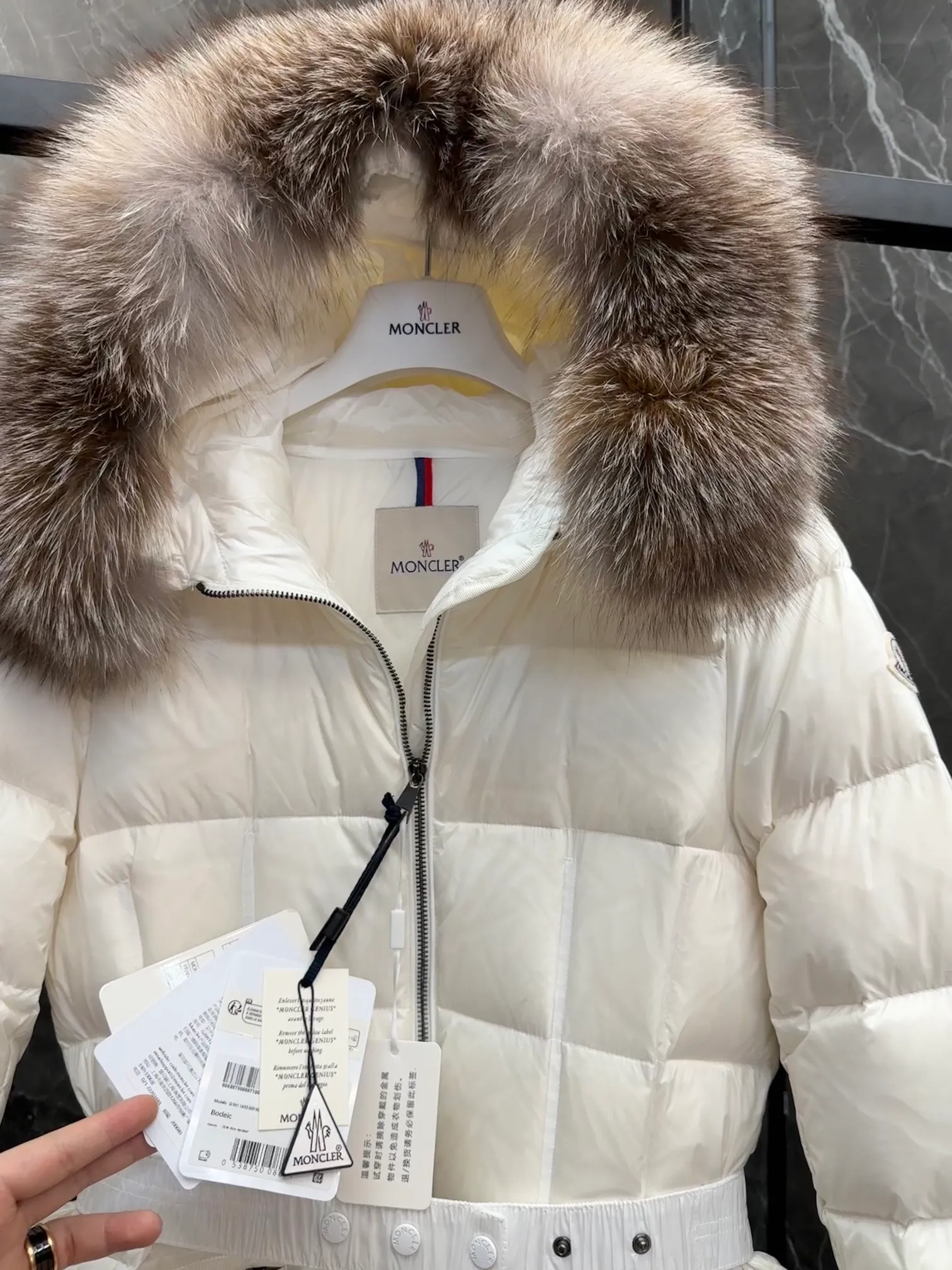 P1020 Moncler Boedic long down jacket for women. (Classic fox fur collar) adopts a whole fox fur collar imported from Finland. The Boedic long down jacket combines exquisite materials and attention to details. The timeless and elegant fashion design can provide you with a warm and caring wearing experience.  Boedic's long down jacket features a waist-cinching belt to accentuate its feminine silhouette for a stylish winter look. The cozy hood has rich fleece trim and is easily removable to suit your mood and weather conditions. Details •Made from lounge saison fabric •Longue saison lining •Filled with down •Hood with removable fox fur collar trim •Two-way zip closure •Elastic waistband with snap button closure •Zip pockets with grosgrain detail •Elastic cuffs Size : 1-4