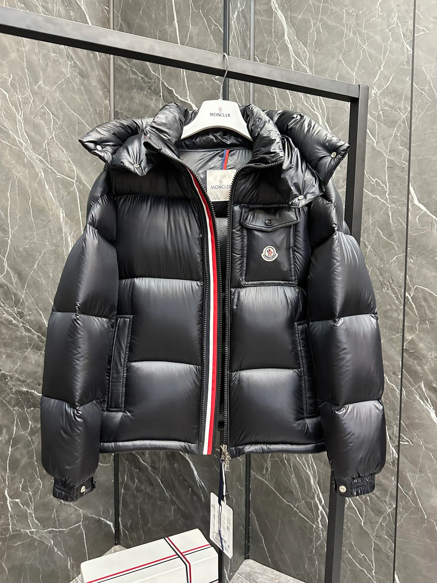 P740 ⬆️Moncler Montbeliard Short Men's Down Jacket Jacket Montbeliard Men's Short Down Jacket has warmth and protection functions, highlighting the fashionable Moncler aesthetic, and is a popular product. The Montbeliard down jacket is made from shiny patented nylon and features recognizable rectangular quilting. Featuring a hooded design and signature patch pocket at chest. Details •Made from nylon laqué fabric •Nylon laqué lining •Filled with down •Removable and adjustable hood with drawstring closure •Internal flap with webbing •Black pocket detail at lower end •Zipper closure •Snap-button closure at collar •Zipper pockets •Push-button closure at patch pockets •Adjustable cuffs •Adjustable elastic drawstring hem Size: 1-5 Couple's Black D9875067650