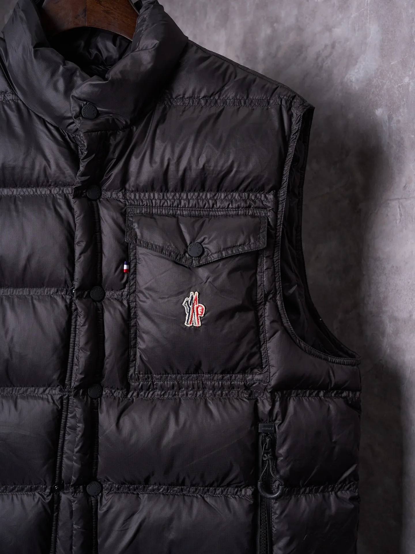 P680 Actual hanging auction] MONCLER/Mandow embroidered reflective logo stand-up collar down vest [Ready stock] 1 2 3 4 It is made of extremely fine nylon yarn and woven in a high-density way. The number of yarns per unit area is large, and the gaps between the yarns are very small, which can effectively block the penetration of cold wind. The fine weave keeps it lightweight and soft to the touch, physically restricting the lightweight down fibers from slipping through the gaps. Nylon fiber itself has good wear resistance and is not easy to snag, which significantly extends its service life and can easily cope with the needs of multiple scenarios.  The lining is made of high-density weaving of 100% polyester fiber, with a thickness of 0.08mm to avoid increasing the overall weight and making it smooth to wear. The high-density weaving structure forms a wind resistance layer to protect the thermal efficiency of the thermal layer from loss. It can withstand the expansion pressure of down and prevent deformation and damage after long-term use.  It uses 90 white duck down with a weight of 130g to ensure excellent thermal insulation performance. After strict screening and processing, the velvet is not easy to get drilled, ensuring durability.  Through the reflective cloth punching process, the logo is regularly arranged on the triangular reflective mark with dozens of small holes, which not only improves functionality but also enhances recognition and aesthetics.
