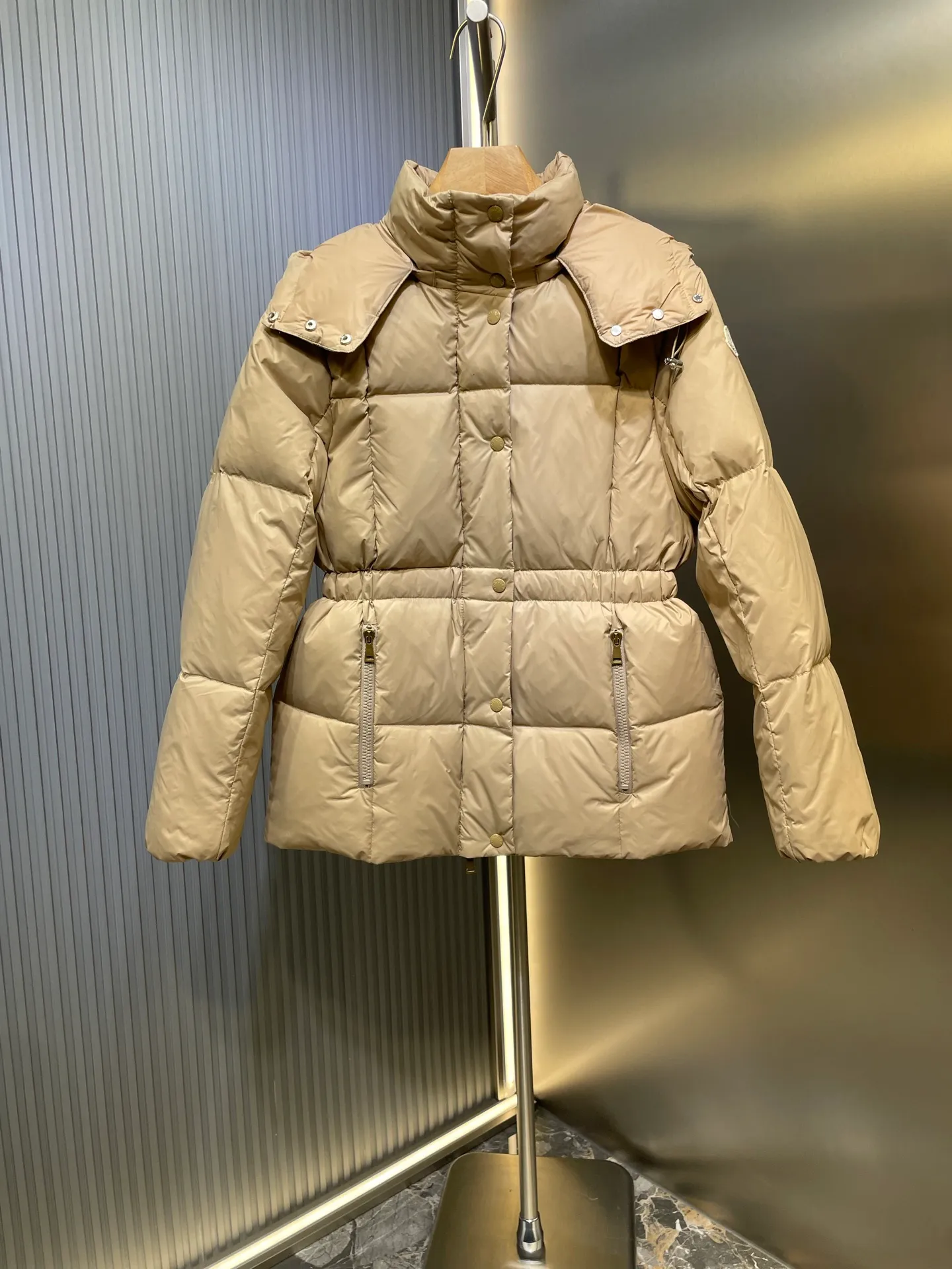 P910 MONCLER 25FW new autumn and winter product. Waisted black gold Agneux women's square quilted hooded short down jacket. The Agneux down jacket combines protective fabrics and exquisite textures. Short fit in functional nylon with a glossy satin finish. Paired with a nipped-in waist design, it outlines a feminine silhouette. Made of nylon Longue saison lining Filled with down Detachable and adjustable hood Zip and snap fastening Zippered pockets Elastic waist Black Apricot Sizes S M L