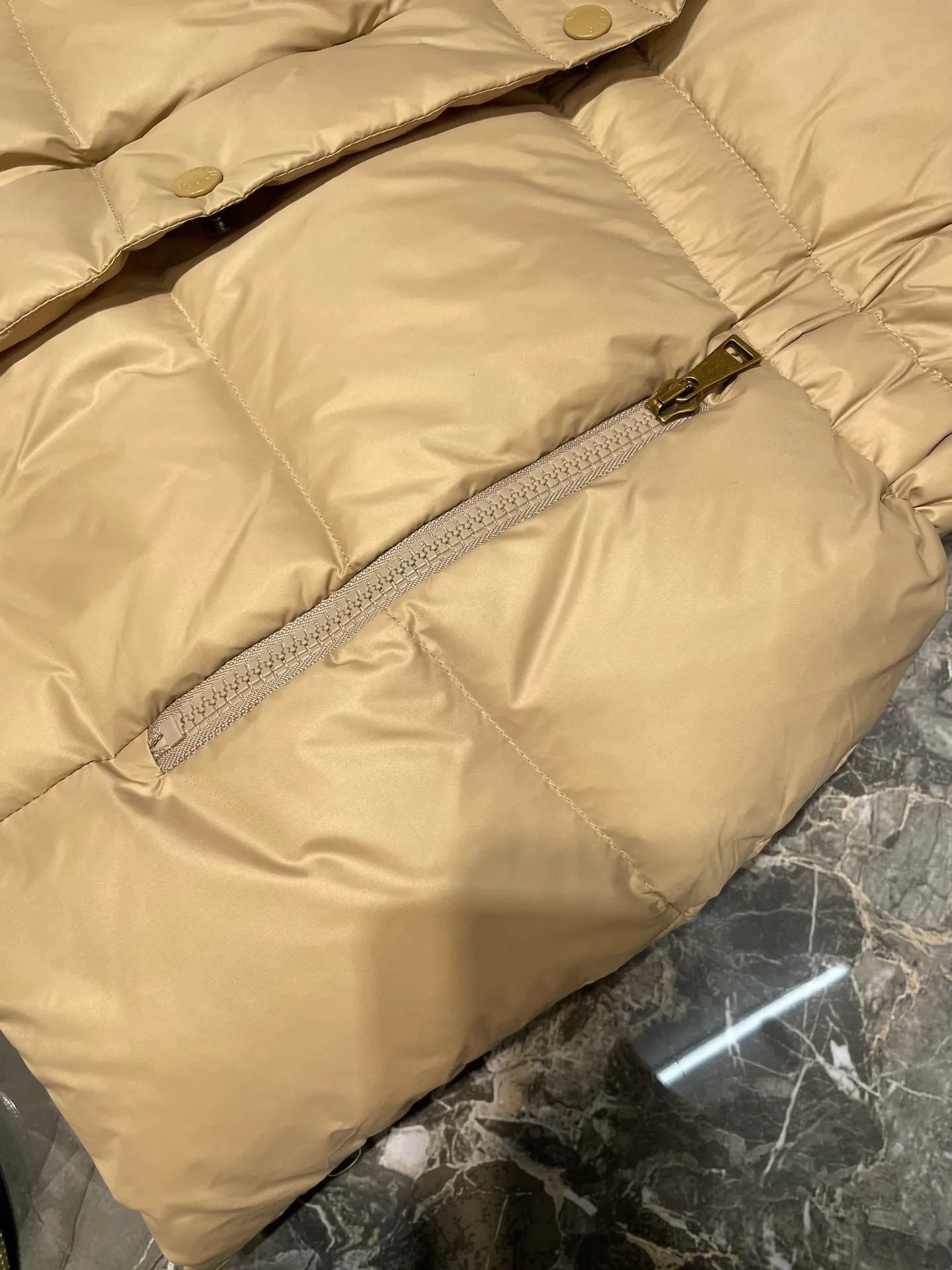 P910 MONCLER 25FW new autumn and winter product. Waisted black gold Agneux women's square quilted hooded short down jacket. The Agneux down jacket combines protective fabrics and exquisite textures. Short fit in functional nylon with a glossy satin finish. Paired with a nipped-in waist design, it outlines a feminine silhouette. Made of nylon Longue saison lining Filled with down Detachable and adjustable hood Zip and snap fastening Zippered pockets Elastic waist Black Apricot Sizes S M L