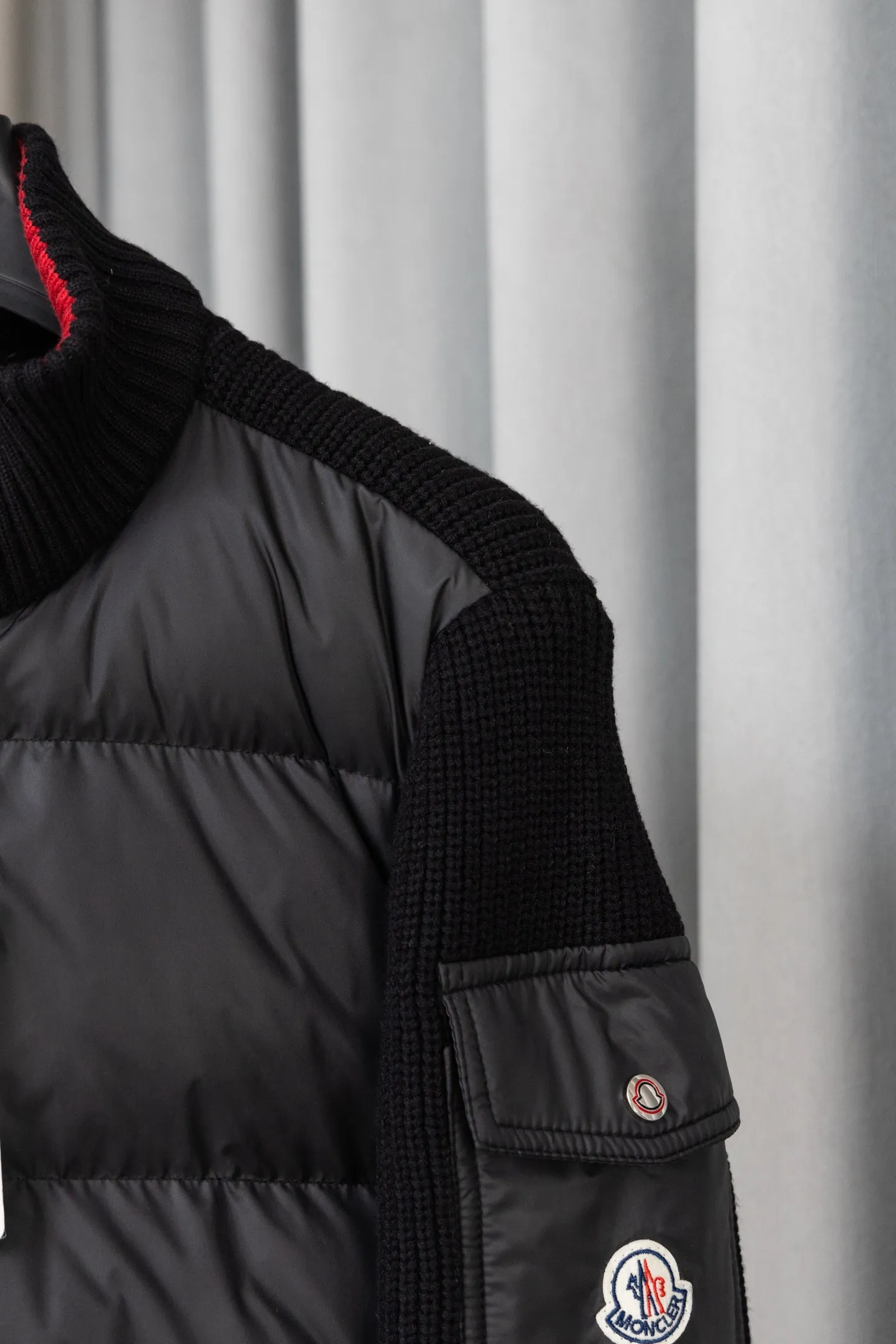 P560 Style number: M046 This is a knitted patchwork down jacket from Moncler. It combines the brand's high-end outdoor genes and fashion design. It is a luxurious item with both warmth and style in autumn and winter. Design highlights: Material splicing: Pure wool knitted sleeves are spliced ​​with a down front filled with 90 white duck down. The knitted part is soft and breathable, and the down part is fluffy and warm, achieving a dual fusion of style and function.  Detailed logo: The iconic Moncler badge pocket on the left arm is a classic embodiment of brand recognition; the stand-up collar design with a two-way zipper not only improves warmth, but also strengthens the neat styling.  Color embellishment: The contrasting red and blue stripes on the cuffs and hem inject vitality into the overall black tone, adding a retro college style charm. Craftsmanship and Quality: The down filling follows the European standard 90 down standard, with excellent fluffiness and down filling, with almost no stiff feeling. At the same time, it adopts the "line first and then separate down filling" process. The four-layer liner effectively prevents down from being drilled, and can maintain warmth even after long-term wear.  The knitted part is made of high-quality wool, which has a delicate touch and is not easily deformed. The splicing process with the down fabric is rigorous, showing a high-end texture level.  Style and Wearing This down jacket is based on the classic college style. The slim straight version can modify the body line and can be easily adapted to a variety of styles: it can be paired with jeans and casual shoes for a casual look on a daily basis. It can also be upgraded to an urban light luxury style by layering it with a turtleneck sweater inside and a suit outside. It is a key item in the winter wardrobe that is both practical and fashionable. Color: black, navy blue, sizes S-XL