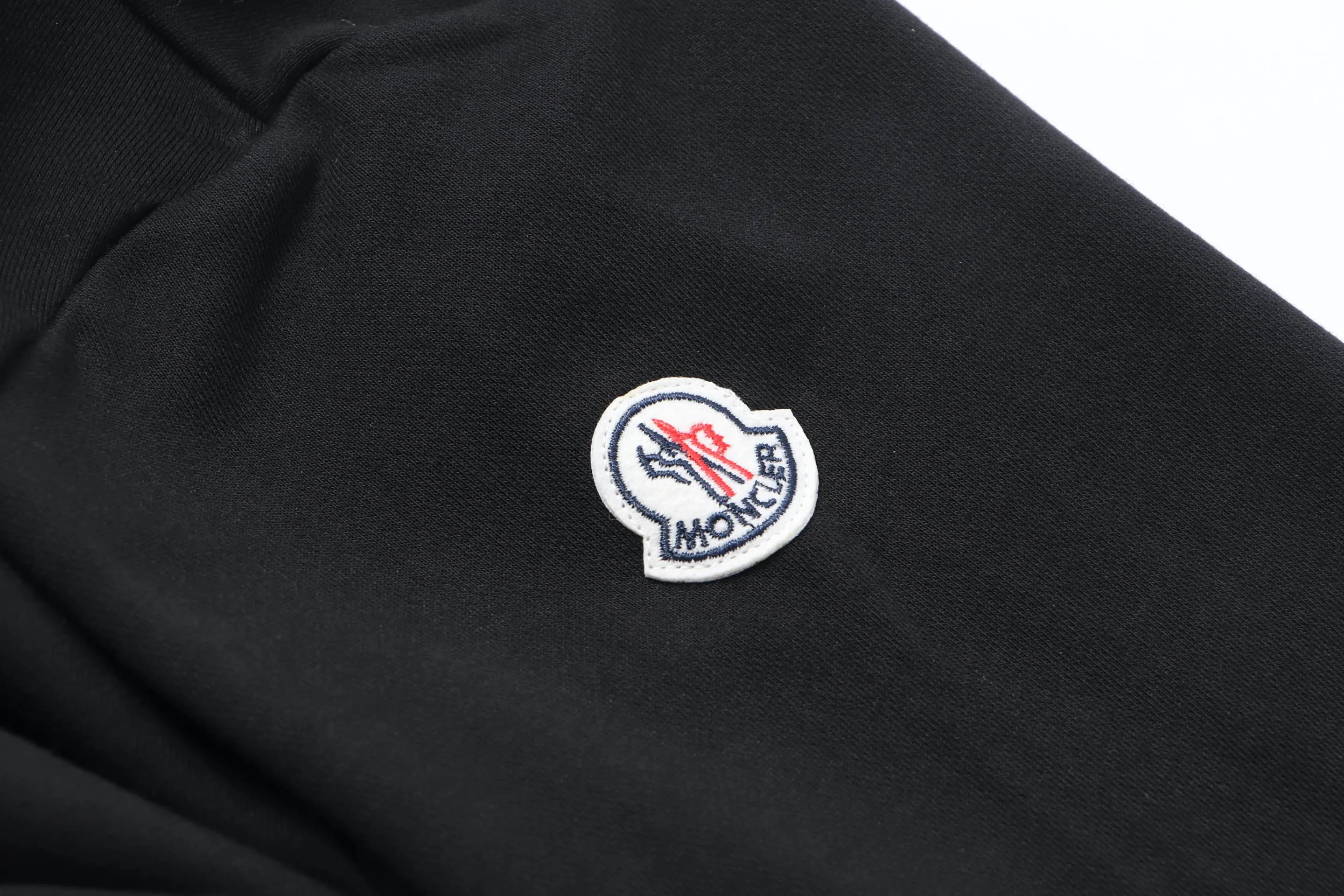 P340 Moncler slogan printed zipper hooded jacket is made of lightweight turned velvet cotton fabric. High-density cotton fiber is used to achieve internal and external differentiation in a single layer of fabric. The outer plain weave is tight and wear-resistant, and the inner layer is sanded to form a short dense suede surface. The dense plain weave structure resists wind and splashes, the brushed suede surface is skin-friendly, and the short pile has been treated to eliminate static electricity to avoid sticking to the skin. A very small amount of grooved polyester moisture-conducting yarn is embedded in the cotton fiber, which quickly guides sweat from the inner suede surface to the outer layer for evaporation through the capillary effect, solving the problem of the suede being easily stuffy. By actively interfering with the shrinkage potential of cotton fibers, the fabric is able to transition from changeable to stable, improving dimensional stability while being less prone to deformation and wrinkles. High saturation is achieved on the center of the cap through glue printing. Size: xs-l