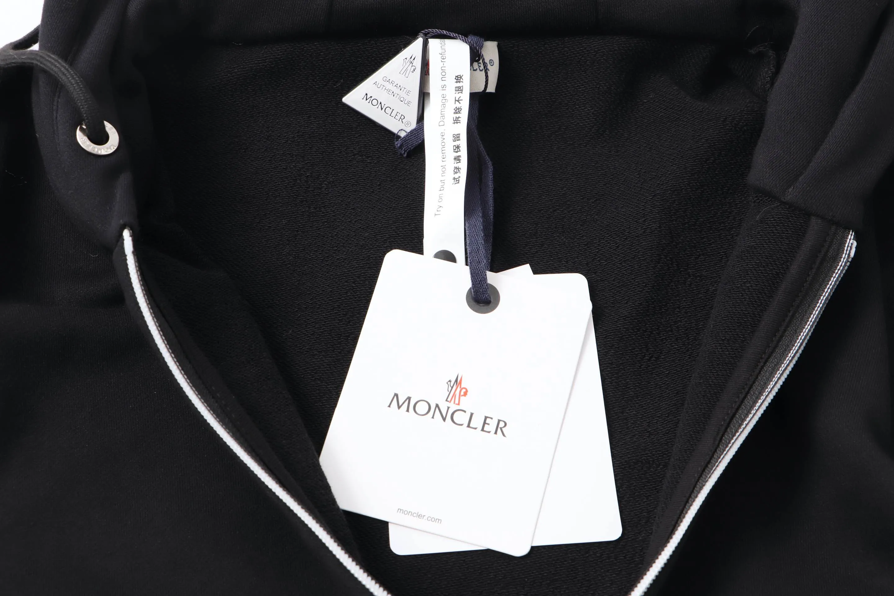 P340 Moncler slogan printed zipper hooded jacket is made of lightweight turned velvet cotton fabric. High-density cotton fiber is used to achieve internal and external differentiation in a single layer of fabric. The outer plain weave is tight and wear-resistant, and the inner layer is sanded to form a short dense suede surface. The dense plain weave structure resists wind and splashes, the brushed suede surface is skin-friendly, and the short pile has been treated to eliminate static electricity to avoid sticking to the skin. A very small amount of grooved polyester moisture-conducting yarn is embedded in the cotton fiber, which quickly guides sweat from the inner suede surface to the outer layer for evaporation through the capillary effect, solving the problem of the suede being easily stuffy. By actively interfering with the shrinkage potential of cotton fibers, the fabric is able to transition from changeable to stable, improving dimensional stability while being less prone to deformation and wrinkles. High saturation is achieved on the center of the cap through glue printing. Size: xs-l