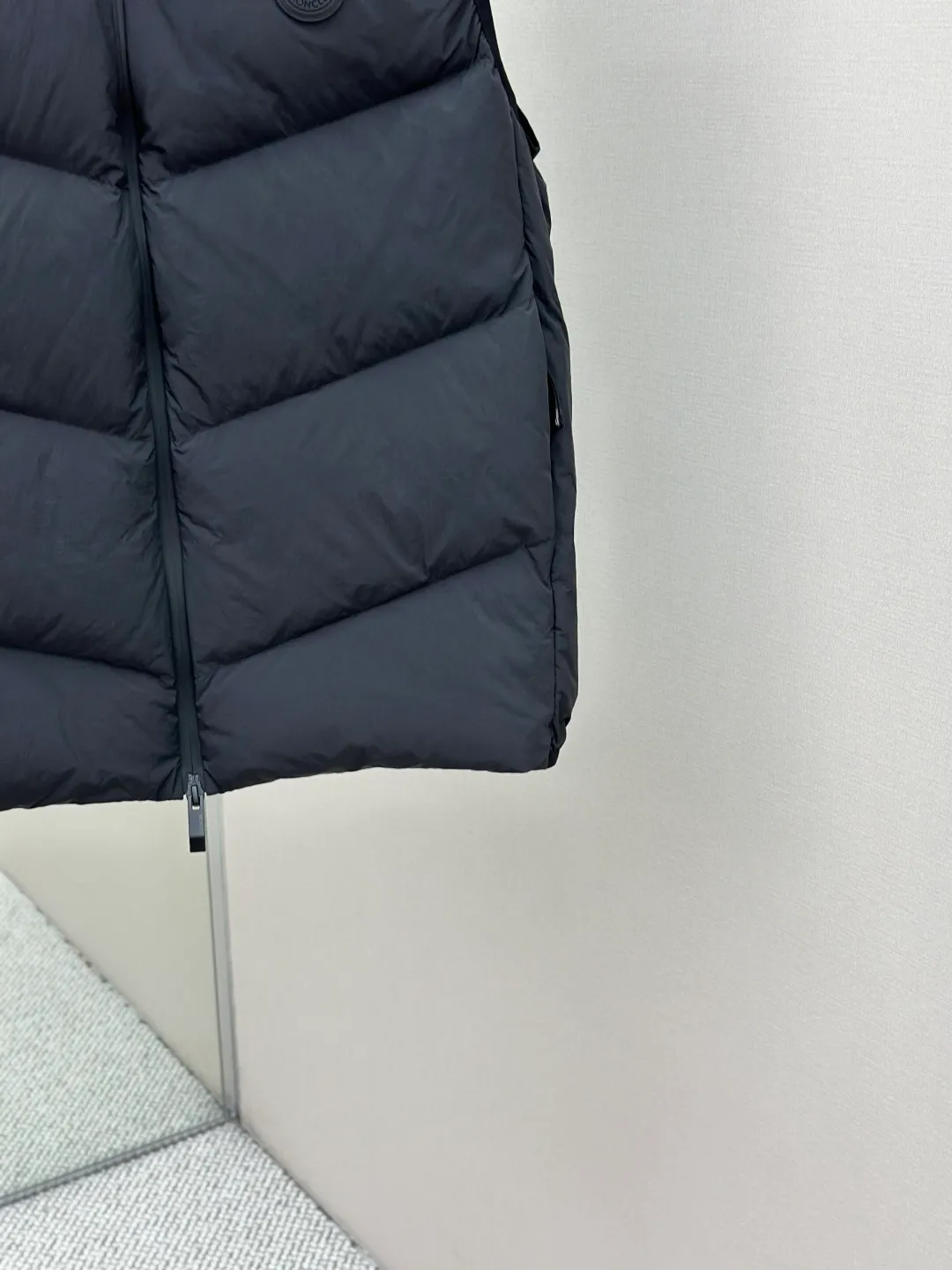 P660 MONCLER Badge Hooded Down Vest Fabric selection: Made of nylon fabric made of 100% nylon, which is woven into a tight and tough fabric through advanced textile technology. It improves the strength of the skeleton to effectively block the invasion of cold wind and lock the warm air generated by the down layer. After tight weaving and special treatment, it has waterproof and windproof functions. The surface forms a certain lotus leaf effect, and is wrinkle-resistant and not easily deformed, making it easy for daily care.  Technology: The quilting stitches are sewn in a diagonal direction at an angle of approximately 70 degrees. The diagonal lines are arranged in parallel. The fabric and filling are planned into different functional areas, and the quilting stitches in each partition are relatively independent. This allows the finished product to produce a larger deformation space along the diagonal direction when stretched and pressed, making it less likely to tighten and break, and has rich visual effects, modern and advanced features.  Details: After the hood is removed, the stand-up collar displays an embossed logo of the same color, adding a unique visual experience and tactile details.  High-quality filling: It is filled with 90% selected white duck down, weighing 170g, ensuring fluffy rebound, lightness and warmth.  Accessories: One-to-one customized zipper pendant, one-to-one customized badge, one-to-one customized three-label SIZE: 1 2 3 4