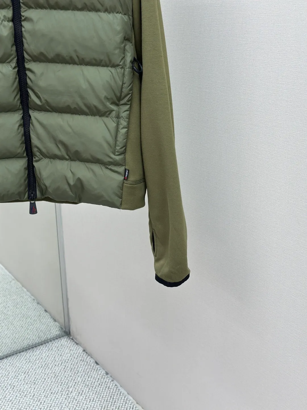 P810 Moncler logo woven splicing down jacket, customized matte crystal lattice air shield velvet and 300D high-density calendered coating, using the new national standard 90 white duck down (welcome to test), full of down, full of warmth, light and fluffy, with the dark green of the overlapping mountains as the background color, all things accumulating, creating its own scenery in silence The Monlcer triangle logo is embellished on the chest, the power aesthetics of the minimalist logo The concentrated down filling in the front area creates dynamic insulation for the core heat dissipation zone of the human body. The hooded down is a moving warm flow barrier for the head and neck, forming a thermal energy circulation system with the front area. The elastic woven sleeves provide freedom of movement with a sense of compression, forming a relaxed and warm philosophy. The real high-end is to let function become the footnote of style. Process 1: Computer mechanical down filling. Prioritize the liner pattern by making a pattern to determine the down filling area and determine the weight of down per square meter according to the original three-dimensional effect. Thus, the amount of down filling for each cut piece is calculated. The computer down filling machine uses a digital weighing unit to achieve stable measurement. Process 2: 3D three-dimensional quilting technology. With the programming system of the CNC quilting machine, the down in different areas is accurately separated to ensure that the filling is evenly fixed after sewing and avoid agglomeration or displacement. Process 3: Computer template machine line running process. The computer template machine line line process shows extremely high neatness and smoothness. The craftsman's precise control of the size during the operation ensures that each line meets the design requirements. The lines of the entire template are smooth and unified, neat and beautiful. Process 4: Triple locking five-thread dense stitching process. Main seam locking + diagonal reinforcement + raw edge wrapping. Triple structure. Forming a three-dimensional protective net at the edge of the fabric to avoid stitch breakage. Paving materials: Customized Moncler zippers. Customized Moncler rope loops. Customized Moncler logo. Customized Moncler eyelets. Customized Moncler trademark. Size: S M L XL