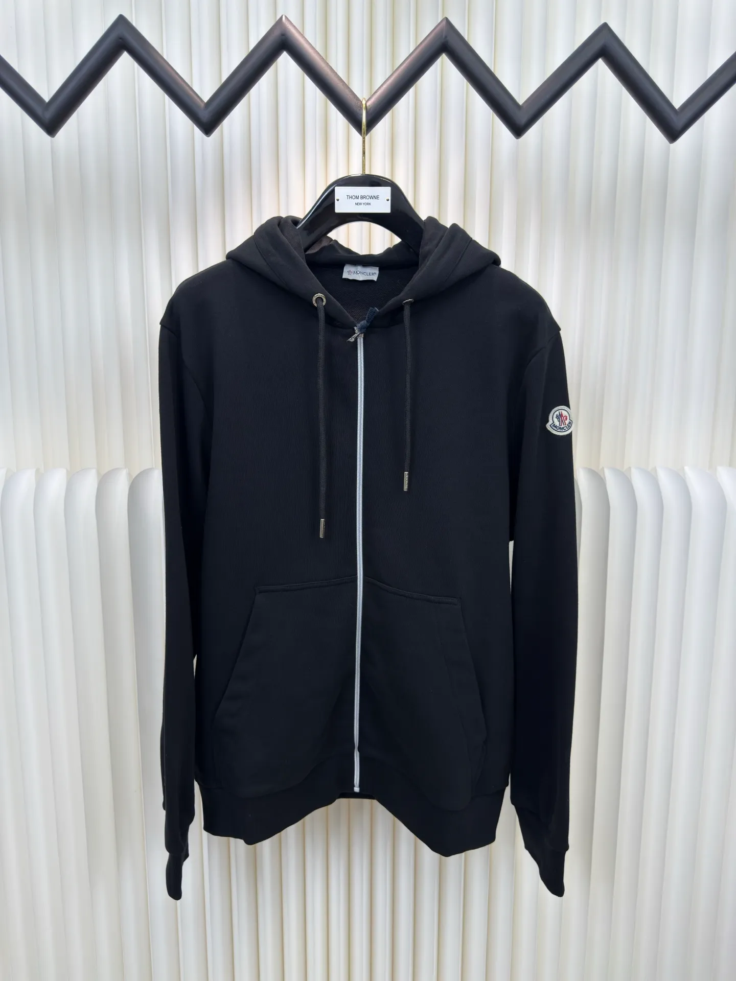P500 MONCLER printed logo hooded sweatshirt is made of lightweight turned-over velvet cotton fabric. High-density cotton fiber is used to achieve internal and external differentiation in a single layer of fabric. The outer plain weave is tight and wear-resistant, and the inner layer is sanded to form a short dense suede surface. The dense plain weave structure resists wind and splashes, the brushed suede surface is skin-friendly, and the short pile has been treated to eliminate static electricity to avoid sticking to the skin. A very small amount of grooved polyester moisture-conducting yarn is embedded in the cotton fiber, which quickly directs sweat from the inner suede surface to the outer layer for evaporation through the capillary effect, solving the problem that the inside-out suede is prone to stuffiness. By actively intervening in the shrinkage potential of the cotton fiber, the fabric is achieved from being volatile to stable, improving dimensional stability, and at the same time not prone to deformation and wrinkles.   A high-saturation pattern is displayed on the center of the cap through glue printing. The scraper pressure is even and the scraping is performed in 5 steps to ensure that the glue is fully penetrated and covered. After curing at high temperature, the pigment is firmly combined with the cotton fiber. The ink absorption and penetration characteristics of the cotton fiber make the pattern less likely to fall off due to friction. Size S M L XL
