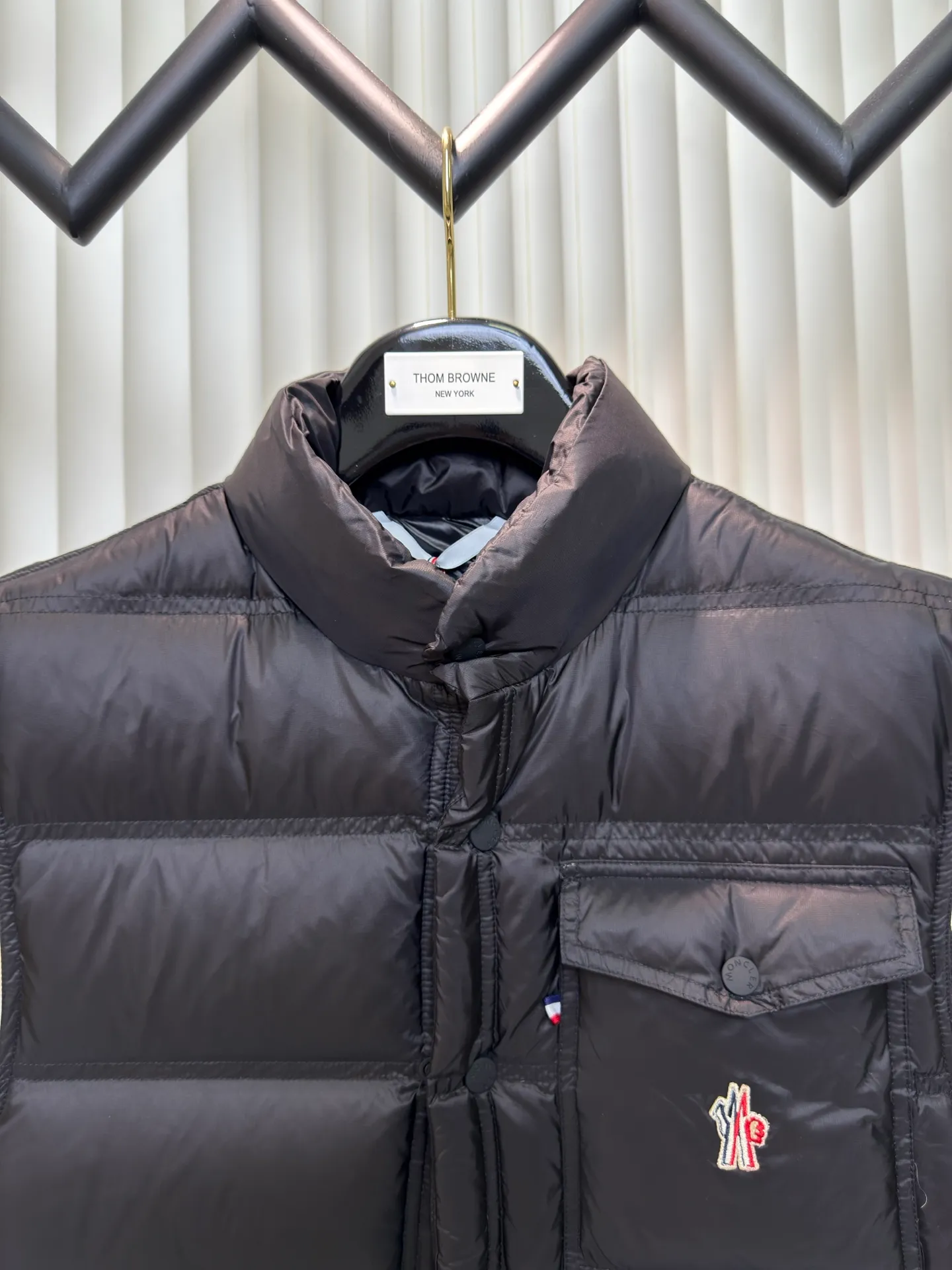 P700 MONCLER masked down vest with reflective markings is made of 90 white duck down with a weight of 130g to ensure excellent thermal insulation performance. After strict screening and processing, the velvet is not easy to get drilled, ensuring durability.  It is made of extremely fine nylon yarn and is woven in a high-density manner. The number of yarns per unit area is large, and the gaps between the yarns are very small, which can effectively block the penetration of cold wind. The fine weave keeps it lightweight and soft to the touch, physically restricting the lightweight down fibers from slipping through the gaps. Nylon fiber itself has good wear resistance and is not easy to snag, which significantly extends its service life and can easily cope with the needs of multiple scenarios.  The lining is made of high-density weaving of 100% polyester fiber, with a thickness of 0.08mm to avoid increasing the overall weight and making it smooth to wear. The high-density weaving structure forms a wind resistance layer to protect the thermal efficiency of the thermal layer from loss. It can withstand the expansion pressure of down and prevent deformation and damage after long-term use.  Through the reflective cloth punching process, the logo is regularly arranged on the triangular reflective mark with dozens of small holes, which not only improves functionality but also enhances recognition and aesthetics. Size 1 2 3 4