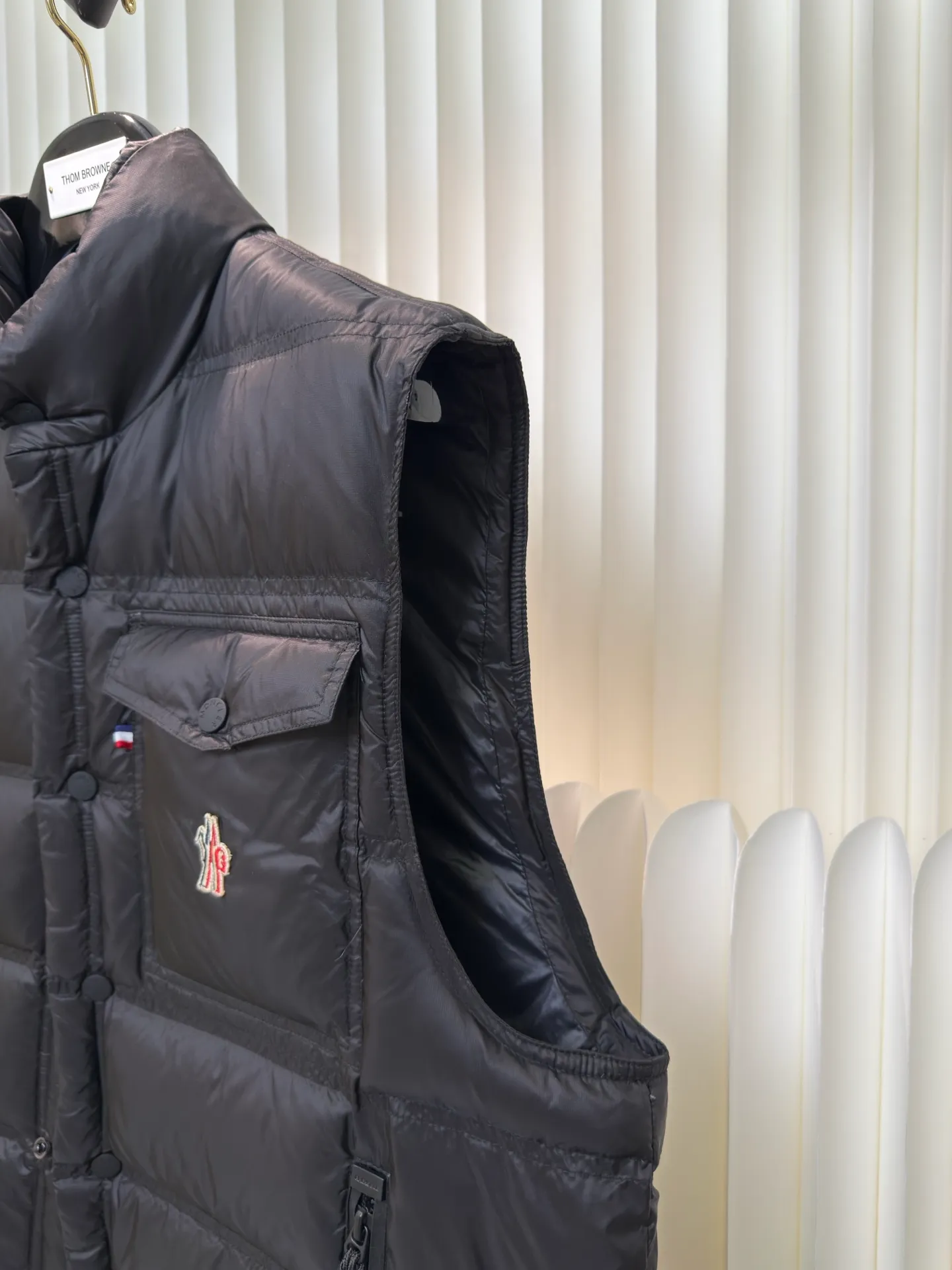 P700 MONCLER masked down vest with reflective markings is made of 90 white duck down with a weight of 130g to ensure excellent thermal insulation performance. After strict screening and processing, the velvet is not easy to get drilled, ensuring durability.  It is made of extremely fine nylon yarn and is woven in a high-density manner. The number of yarns per unit area is large, and the gaps between the yarns are very small, which can effectively block the penetration of cold wind. The fine weave keeps it lightweight and soft to the touch, physically restricting the lightweight down fibers from slipping through the gaps. Nylon fiber itself has good wear resistance and is not easy to snag, which significantly extends its service life and can easily cope with the needs of multiple scenarios.  The lining is made of high-density weaving of 100% polyester fiber, with a thickness of 0.08mm to avoid increasing the overall weight and making it smooth to wear. The high-density weaving structure forms a wind resistance layer to protect the thermal efficiency of the thermal layer from loss. It can withstand the expansion pressure of down and prevent deformation and damage after long-term use.  Through the reflective cloth punching process, the logo is regularly arranged on the triangular reflective mark with dozens of small holes, which not only improves functionality but also enhances recognition and aesthetics. Size 1 2 3 4