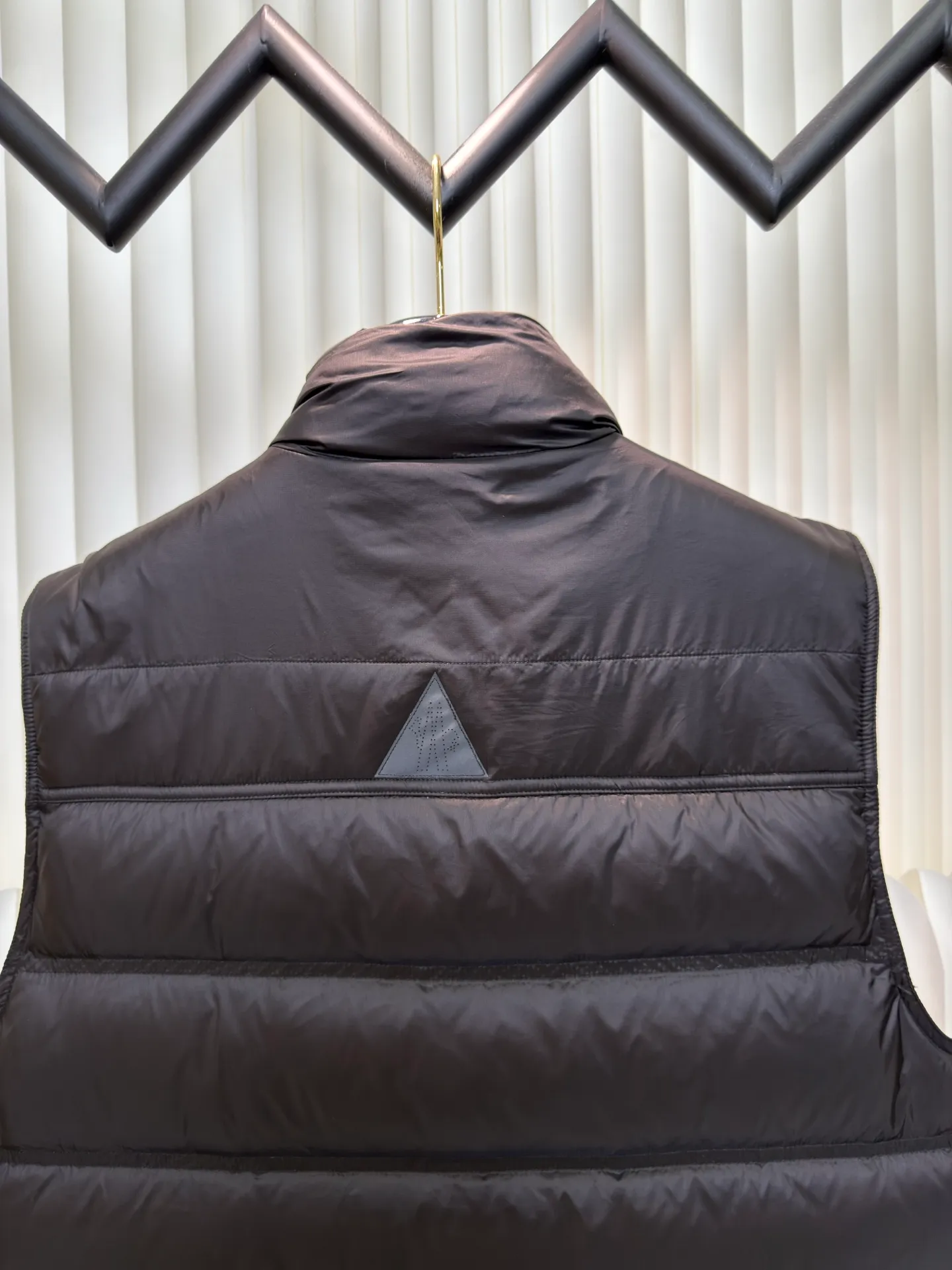 P700 MONCLER masked down vest with reflective markings is made of 90 white duck down with a weight of 130g to ensure excellent thermal insulation performance. After strict screening and processing, the velvet is not easy to get drilled, ensuring durability.  It is made of extremely fine nylon yarn and is woven in a high-density manner. The number of yarns per unit area is large, and the gaps between the yarns are very small, which can effectively block the penetration of cold wind. The fine weave keeps it lightweight and soft to the touch, physically restricting the lightweight down fibers from slipping through the gaps. Nylon fiber itself has good wear resistance and is not easy to snag, which significantly extends its service life and can easily cope with the needs of multiple scenarios.  The lining is made of high-density weaving of 100% polyester fiber, with a thickness of 0.08mm to avoid increasing the overall weight and making it smooth to wear. The high-density weaving structure forms a wind resistance layer to protect the thermal efficiency of the thermal layer from loss. It can withstand the expansion pressure of down and prevent deformation and damage after long-term use.  Through the reflective cloth punching process, the logo is regularly arranged on the triangular reflective mark with dozens of small holes, which not only improves functionality but also enhances recognition and aesthetics. Size 1 2 3 4