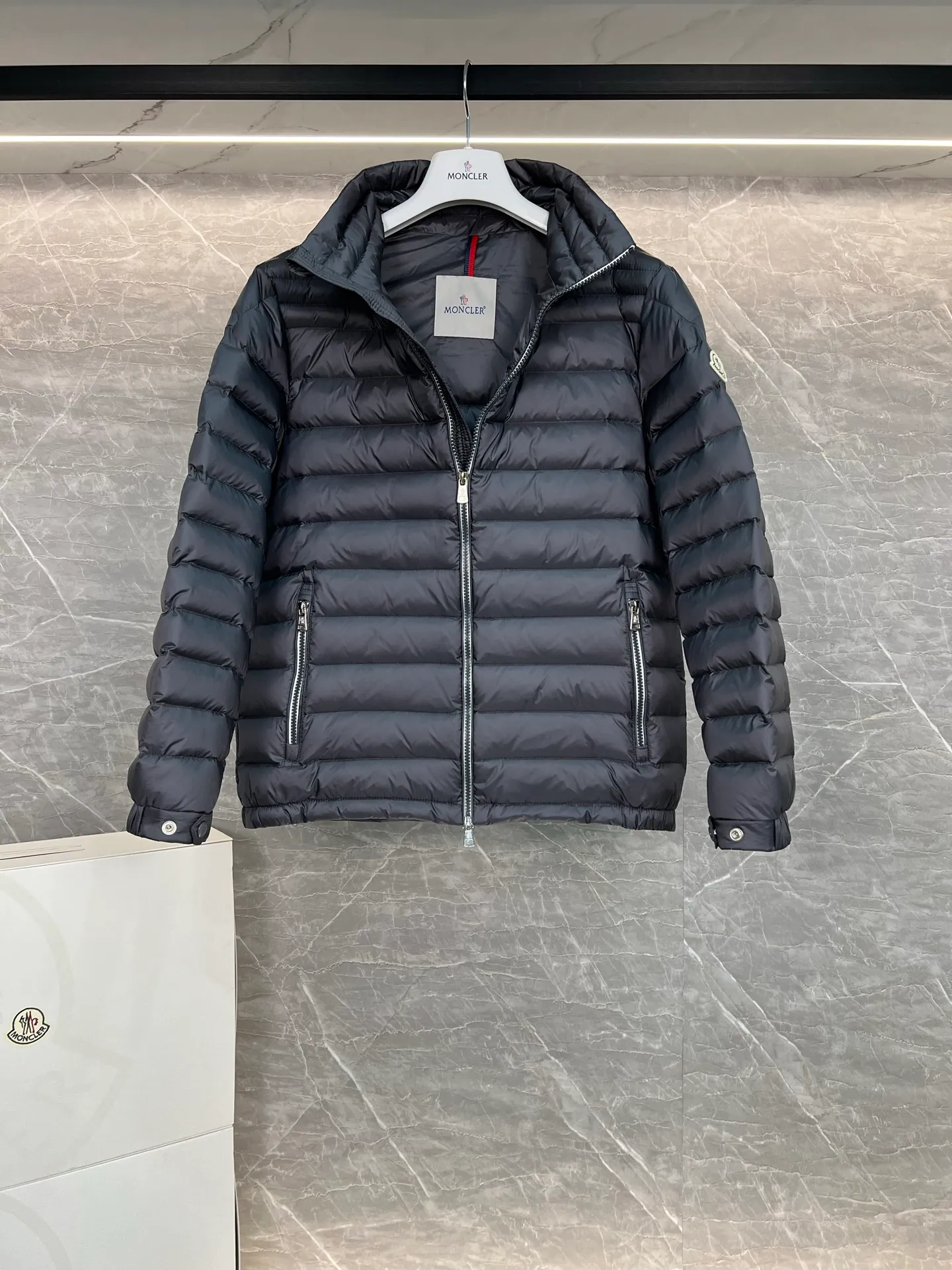 P780 Moncler Arnique short and lightweight men's down jacket. Super soft and delicate fabric, white duck down filling. Extremely lightweight and warm. The Arnique hooded down jacket is made of polyester fiber outer fabric and is Moncler's classic men's design item.  The Arnique short down jacket features classic checkered quilting and signature patch pockets on the sleeves, highlighting the Moncler style. The outer fabric reflects the brand's commitment to lowering its environmental footprint. Modular design, removable hood can be easily put on and taken off according to weather conditions. Details Made of polyester outer fabric Polyester lining Filled with down Size: 1-5 Silver Gray Black