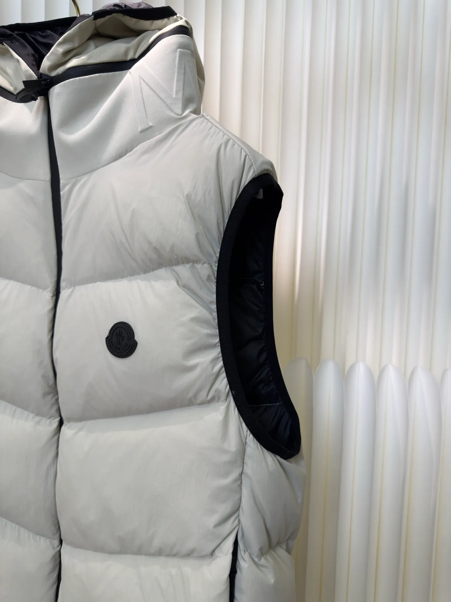 P660 MONCLER Badge Hooded Down Vest is made of nylon fabric made of 100% nylon. It is woven into a tight and tough fabric through advanced textile technology. It improves the strength of the frame and effectively blocks the invasion of cold wind and locks in the warm air generated by the down layer. After tight weaving and special treatment, it is waterproof and windproof. The surface forms a certain lotus leaf effect. It is also wrinkle-resistant and not easy to deform, making it easy for daily care.  The quilting stitches are sewn in a diagonal direction at an angle of about 70 degrees, and the diagonal lines are arranged in parallel. The fabric and filling are planned into different functional areas, and the quilting stitches in each partition are relatively independent. This allows the finished product to produce a larger deformation space along the diagonal direction when stretched and pressed, making it less likely to tighten and break, and has rich visual effects, modern and advanced features.  After the hood is removed, the stand-up collar displays an embossed logo of the same color, adding a unique visual experience and tactile details. High-quality filling: It is filled with 90% selected white duck down, weighing 170g, ensuring fluffy rebound, lightness and warmth. Size 1 2 3 4