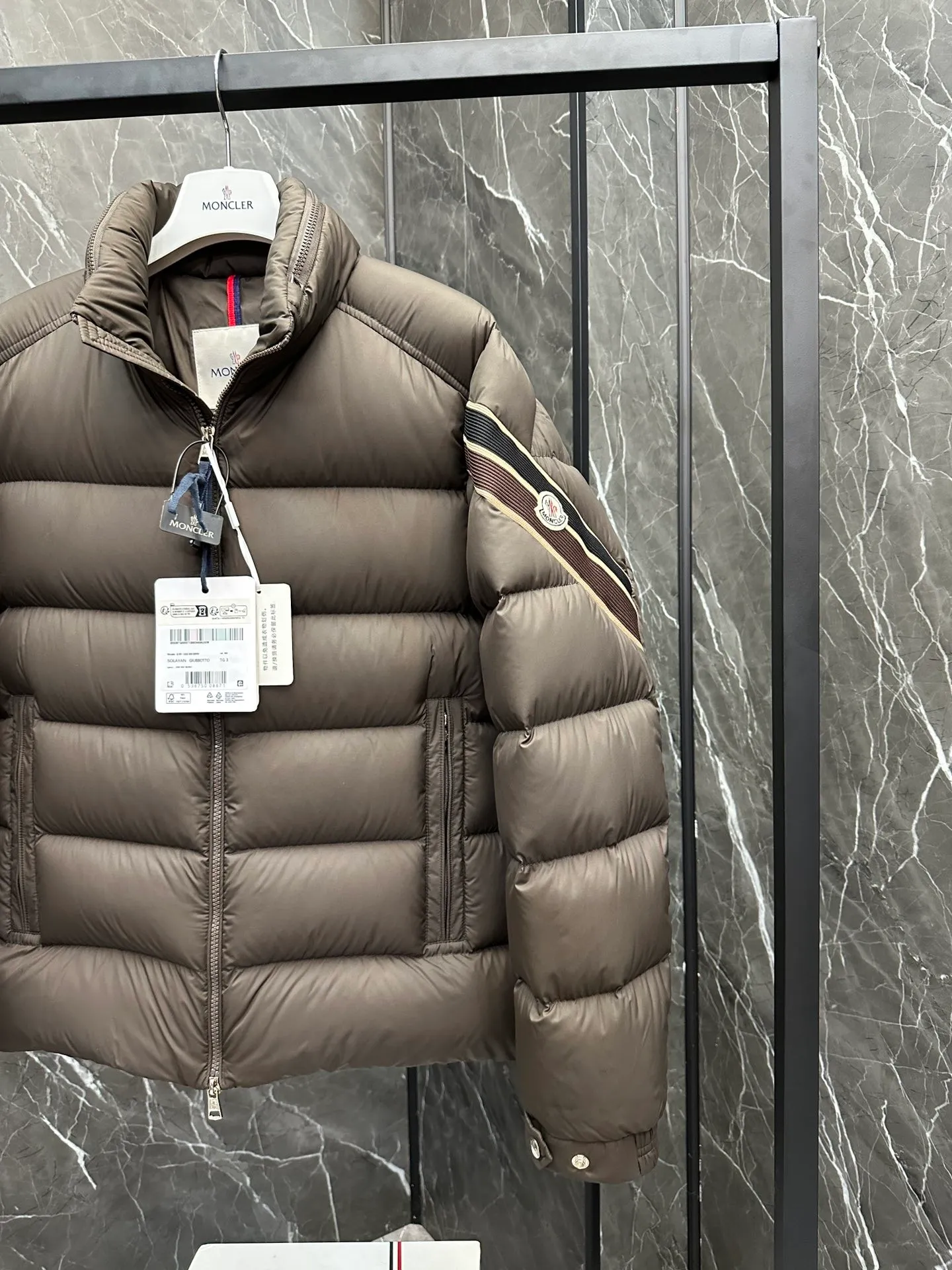 P920 2024N haute couture down moncler solayan men's three-color trimmed short down. Premium goose down filling. The most delicate, lightest and neatest fabric. Solayan men's short down is decorated with seasonal iconic stripe details, blending sportsmanship and timeless style. Solayan down is made of micro chic fabric and has a tough square shape design, highlighting Moncler's sporty spirit. This cropped style has tricolor stripes on the sleeves, a seasonal take on the brand's signature. Comes with a practical pull-out hood. Details · Made of micro chic nylon fabric · Micro chic nylon lining · Filled down · Pull-out hood · Zipper closure · Zipper pocket · Adjustable cuffs · Elastic drawstring hem · Tri-color trim on sleeves size: 1-5 Color: white, dark brown, black