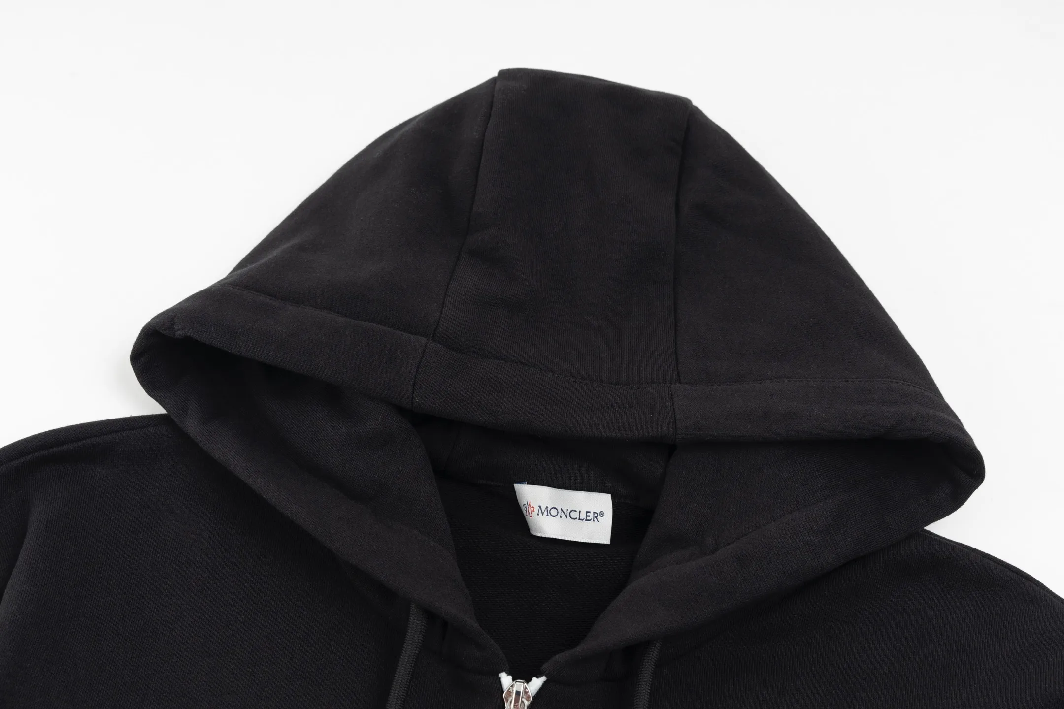 P480 Exclusive supply] Moncler slogan printed zipper hooded jacket is made of lightweight turned velvet cotton fabric. High-density cotton fiber is used to achieve internal and external differentiation in a single layer of fabric. The outer plain weave is tight and wear-resistant, and the inner layer is formed into a short dense suede surface through a sanding process. The dense plain weave structure resists wind and splashes, the brushed suede surface is skin-friendly, and the short pile has been treated to eliminate static electricity to avoid sticking to the skin. A very small amount of grooved polyester moisture-conducting yarn is embedded in the cotton fiber, which quickly guides sweat from the inner suede surface to the outer layer for evaporation through the capillary effect, solving the problem of the suede being easily stuffy. By actively interfering with the shrinkage potential of cotton fibers, the fabric is able to transition from changeable to stable, improving dimensional stability while being less prone to deformation and wrinkles. A high-saturation pattern is displayed on the center of the cap through glue printing. The scraper pressure is even and the scraping is performed in 5 steps to ensure that the glue is fully penetrated and covered. After curing at high temperature, the pigment is firmly bonded to the cotton fiber. The ink-absorbing and penetrating properties of the cotton fiber make the pattern less likely to fall off due to friction. Size:S/M/L/XL