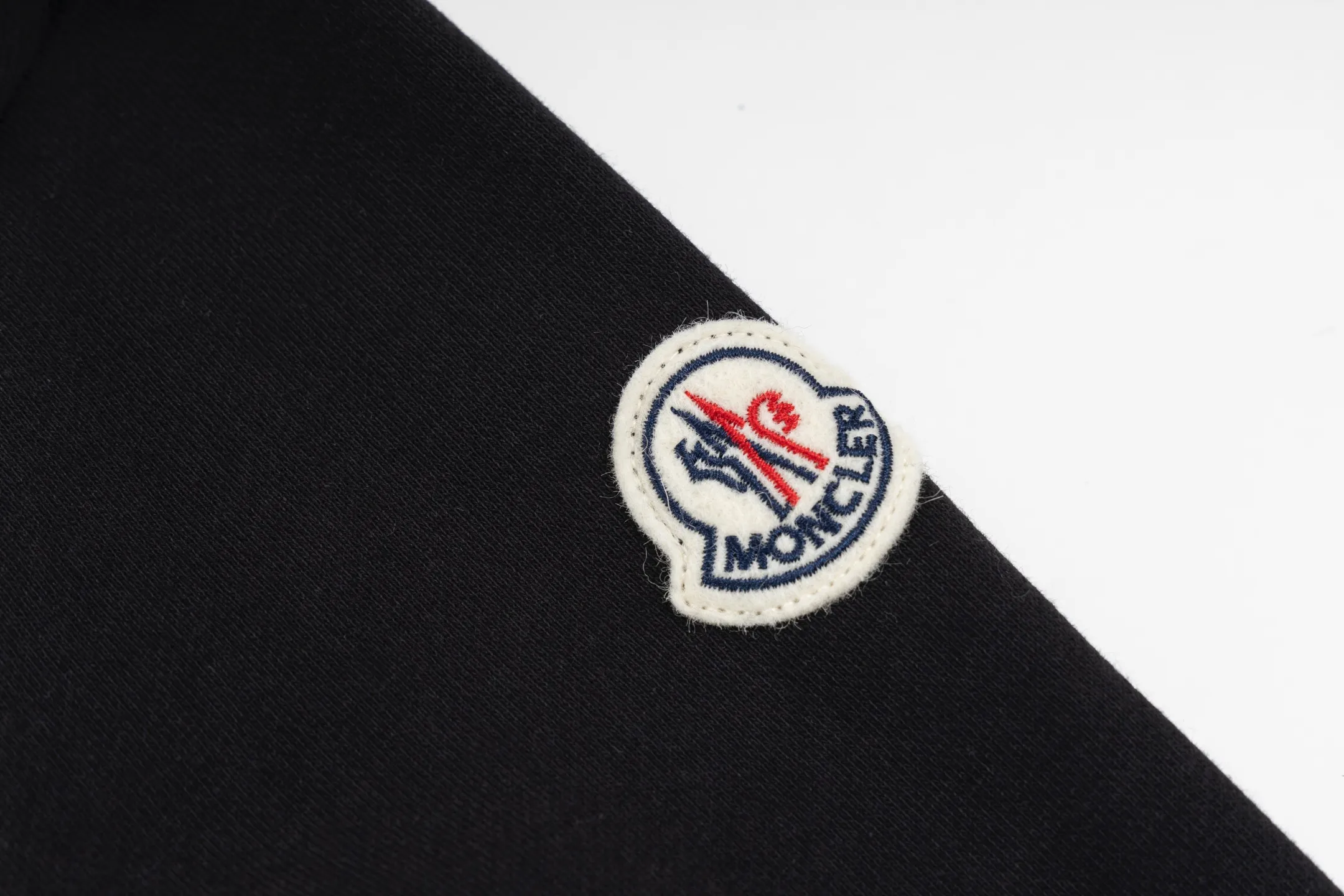 P480 Exclusive supply] Moncler slogan printed zipper hooded jacket is made of lightweight turned velvet cotton fabric. High-density cotton fiber is used to achieve internal and external differentiation in a single layer of fabric. The outer plain weave is tight and wear-resistant, and the inner layer is formed into a short dense suede surface through a sanding process. The dense plain weave structure resists wind and splashes, the brushed suede surface is skin-friendly, and the short pile has been treated to eliminate static electricity to avoid sticking to the skin. A very small amount of grooved polyester moisture-conducting yarn is embedded in the cotton fiber, which quickly guides sweat from the inner suede surface to the outer layer for evaporation through the capillary effect, solving the problem of the suede being easily stuffy. By actively interfering with the shrinkage potential of cotton fibers, the fabric is able to transition from changeable to stable, improving dimensional stability while being less prone to deformation and wrinkles. A high-saturation pattern is displayed on the center of the cap through glue printing. The scraper pressure is even and the scraping is performed in 5 steps to ensure that the glue is fully penetrated and covered. After curing at high temperature, the pigment is firmly bonded to the cotton fiber. The ink-absorbing and penetrating properties of the cotton fiber make the pattern less likely to fall off due to friction. Size:S/M/L/XL