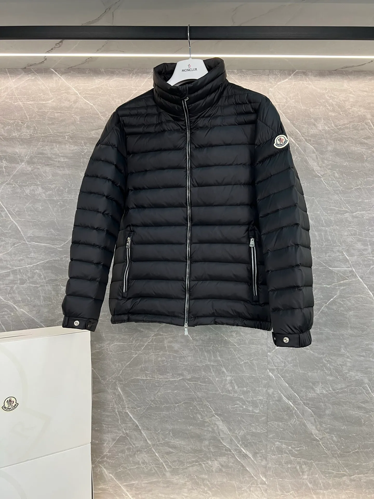 P780 Moncler Arnique short and lightweight men's down jacket. Super soft and delicate fabric, white duck down filling. Extremely lightweight and warm. The Arnique hooded down jacket is made of polyester fiber outer fabric and is Moncler's classic men's design item.  The Arnique short down jacket features classic checkered quilting and signature patch pockets on the sleeves, highlighting the Moncler style. The outer fabric reflects the brand's commitment to lowering its environmental footprint. Modular design, removable hood can be easily put on and taken off according to weather conditions. Details Made of polyester outer fabric Polyester lining Filled with down Size: 1-5 Silver Gray Black