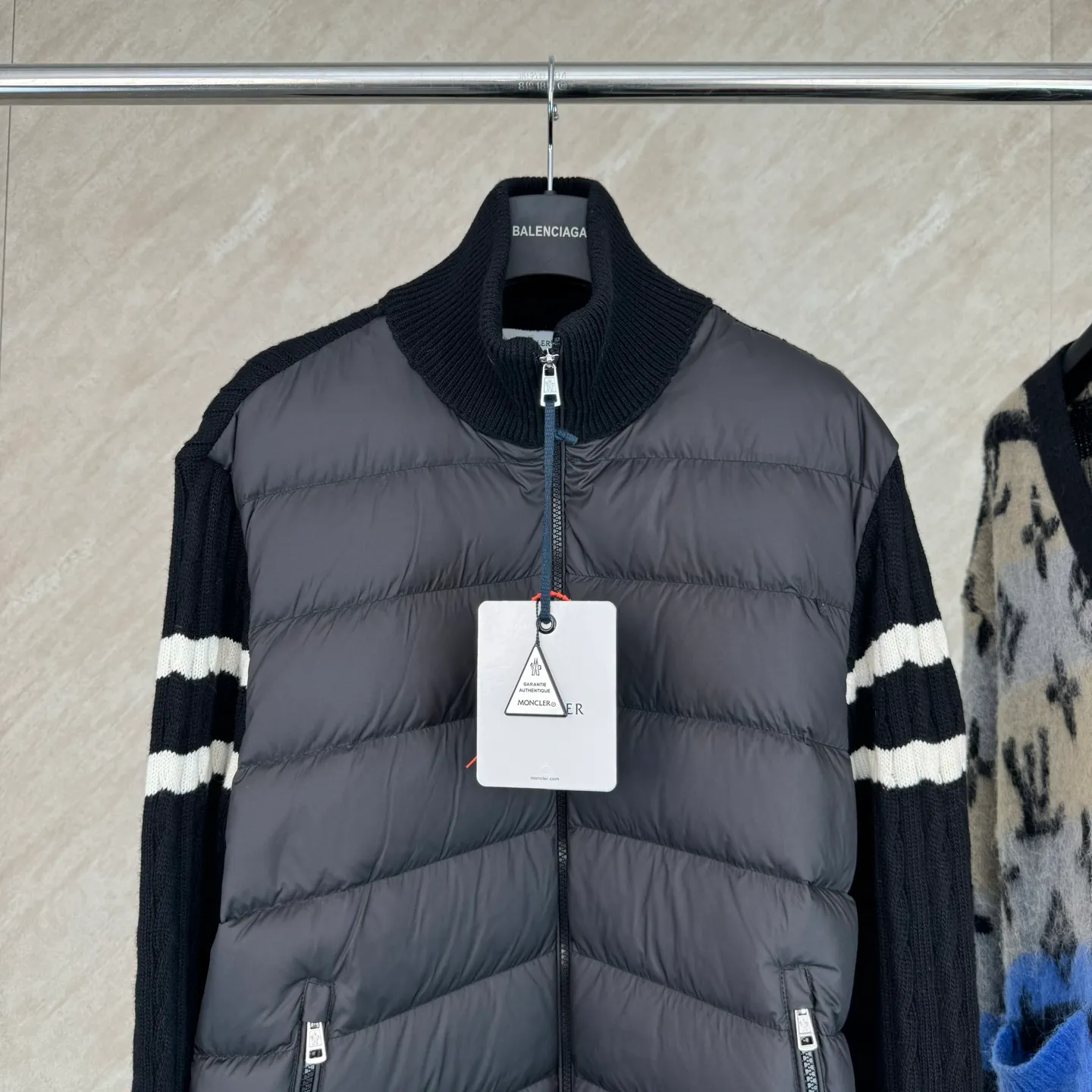 P810 Moncler Mouth Woolen Spliced ​​Down Jacket Size: 1 2 3 4 Fabric Selection: The outer front fabric is made of 100% nylon (nylon). Its high-density structure achieves excellent windproof effect. It also has strong wear resistance and wrinkle resistance. It is not afraid of scratches in daily wear and is easy to take care of.  The splicing design of sweaters and down jackets not only retains the thermal performance of down jackets, but also incorporates the fashion elements of sweaters, making the overall garment both practical and fashionable.  High-quality material: filled with high-quality white duck down, with a filling capacity of 100g, which has excellent thermal insulation effect. At the same time, the sweater is made of wool, cashmere and other natural fibers, which are soft, comfortable and skin-friendly.  The sweaters and down jackets are carefully spliced ​​to ensure comfortable wearing and are not prone to threading or velvet loss.  High collar design: not only provides excellent thermal insulation effect, but also adds a unique sense of fashion, allowing the wearer to maintain style in the cold season.  Stripe decoration: The stripes on the sleeve arms are like bright brush strokes, embellished on the dark gray down jacket, injecting vitality and movement into the overall look, making the clothing more eye-catching.  Accessories: one-to-one customized zipper puller, one-to-one customized armband