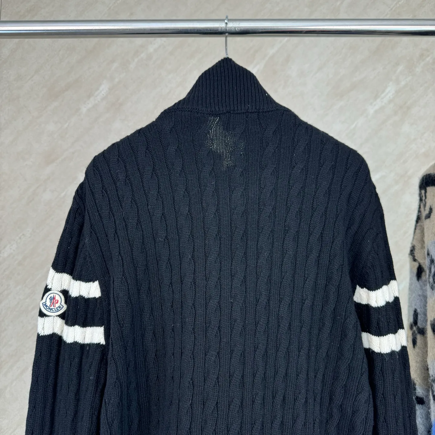 P810 Moncler Mouth Woolen Spliced ​​Down Jacket Size: 1 2 3 4 Fabric Selection: The outer front fabric is made of 100% nylon (nylon). Its high-density structure achieves excellent windproof effect. It also has strong wear resistance and wrinkle resistance. It is not afraid of scratches in daily wear and is easy to take care of.  The splicing design of sweaters and down jackets not only retains the thermal performance of down jackets, but also incorporates the fashion elements of sweaters, making the overall garment both practical and fashionable.  High-quality material: filled with high-quality white duck down, with a filling capacity of 100g, which has excellent thermal insulation effect. At the same time, the sweater is made of wool, cashmere and other natural fibers, which are soft, comfortable and skin-friendly.  The sweaters and down jackets are carefully spliced ​​to ensure comfortable wearing and are not prone to threading or velvet loss.  High collar design: not only provides excellent thermal insulation effect, but also adds a unique sense of fashion, allowing the wearer to maintain style in the cold season.  Stripe decoration: The stripes on the sleeve arms are like bright brush strokes, embellished on the dark gray down jacket, injecting vitality and movement into the overall look, making the clothing more eye-catching.  Accessories: one-to-one customized zipper puller, one-to-one customized armband
