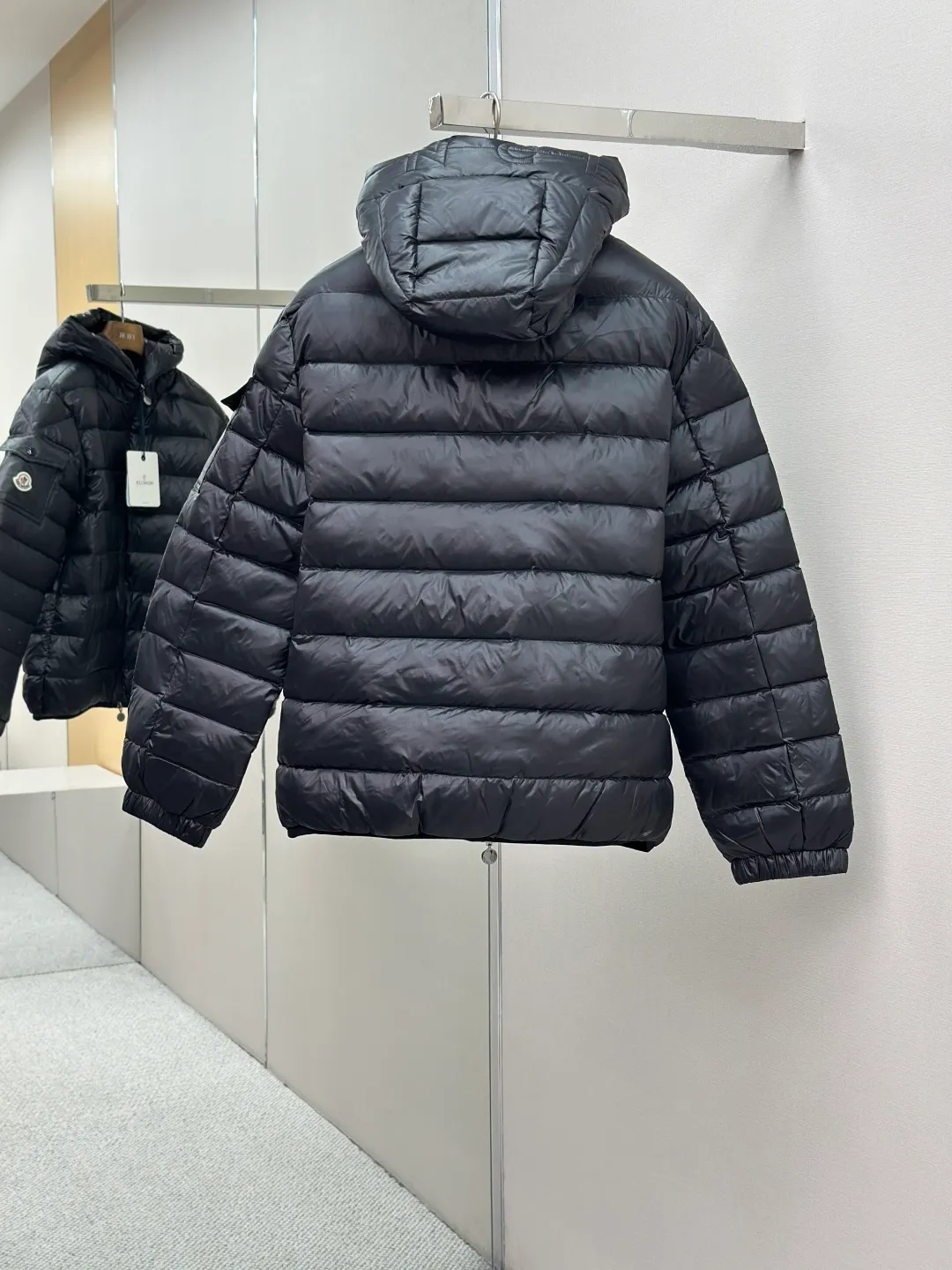 P910 MONCLER hooded brim quilted embroidered down jacket Fabric selection: The longue saison fabric is made of high-count polyamide fiber, which is known for its excellent tensile strength and lightness. Its good flexibility makes the fabric less prone to wrinkles and keeps it crisp and stylish for a long time. The tight weave effectively blocks the invasion of cold wind and locks in the warm air generated by the down layer. The high-density nylon surface forms a certain lotus leaf effect, making it difficult for small water droplets to penetrate, keeping the interior dry and effectively extending the service life of the down.  Lining selection: High-density lining fabric made of ultra-fine denier, 0.08mm thickness to avoid increasing the overall weight and making it smooth to wear. The high-density woven structure forms a wind resistance layer to protect the thermal efficiency of the thermal layer from loss. It can also withstand the expansion pressure of down and prevent deformation and damage after long-term use.  Technology: The quilted letter logo on the brim uses contour quilting technology. The stitching is routed along the edge of the set outline, and the filler is compressed inside the letter graphic, so that the logo is three-dimensional and convex, and the pattern is clear.  High-quality filling: It is filled with 90% selected white duck down, weighing 210g, ensuring fluffy rebound, lightness and warmth.  Accessories: customized zipper pendant, customized badge, customized three-label SIZE: 1 2 3 4
