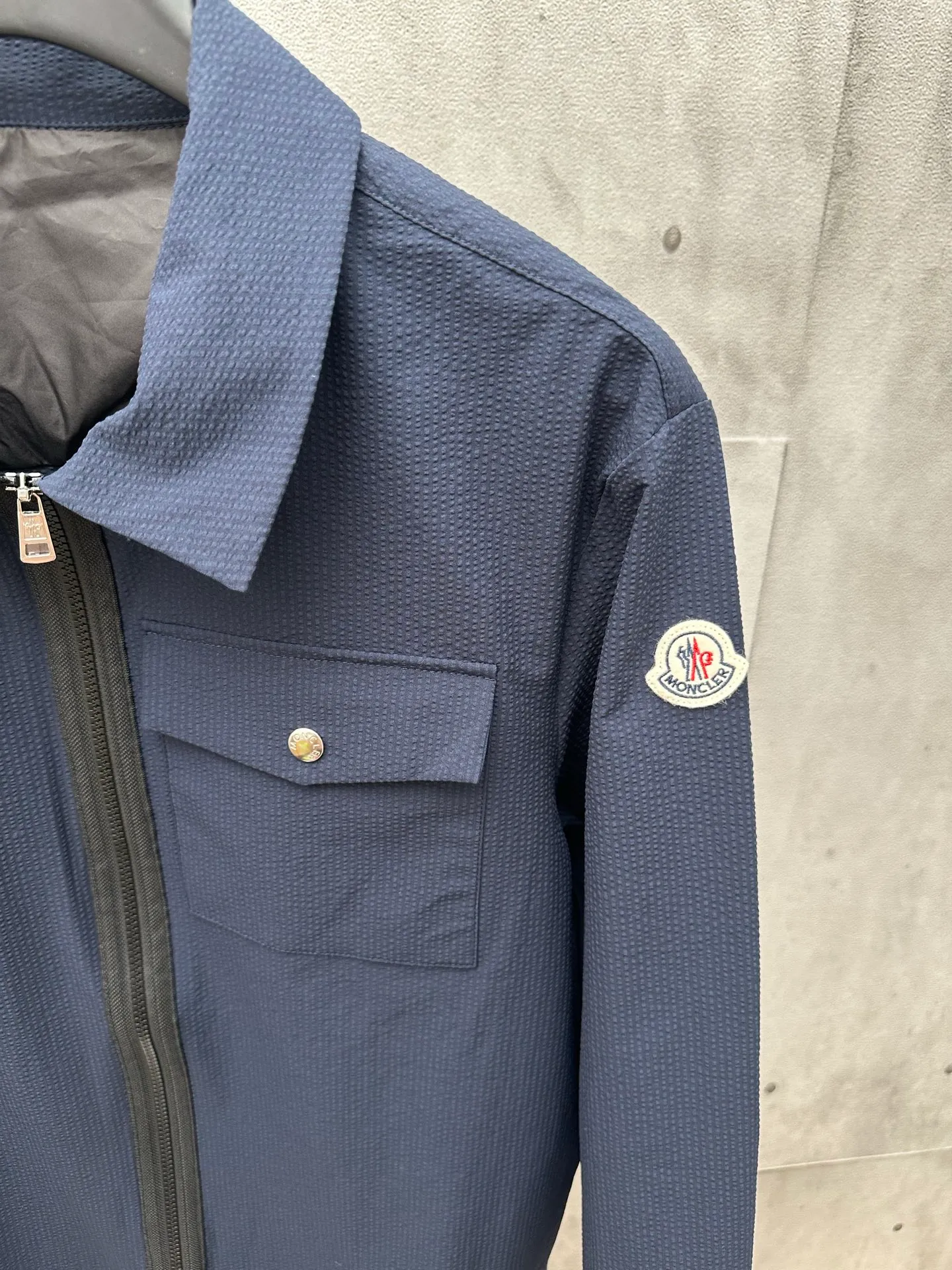 P440 MONCLER bubble wrinkle shirt jacket Fabric selection: Made of cotton blended woven fabric with 76% high cotton content + 24% polyester fiber. The high cotton content ensures that the fabric is soft, skin-friendly, and has good breathability. The addition of a small amount of polyester fiber balances the wrinkle resistance and elasticity of the overall fabric and greatly reduces its shrinkage. After preshrinking, dimensional changes during washing are negligible. The fusion of the two makes the fabric combine anti-wrinkle, quick-drying, easy care and other characteristics without losing the advantages of good wearing experience and strong breathability.  Bubble wrinkle technology: ground warp + bubble warp independent let-off. The bubble warp yarn feeding speed is about 20% higher than the ground warp yarn feeding speed. During weaving, the bubble warp is relaxed and accumulated, forming a naturally arched bubble unit. Through the alternating arrangement of yarns + floating length tissue changes, a clear grid frame is built between the bubble units, and finally the bubble three-dimensional effect and grid outline are locked through high-temperature heat setting.  Accessories: One-to-one customized zipper puller, one-to-one customized LOGO armband, one-to-one customized snap button SIZE: 1 2 3 4