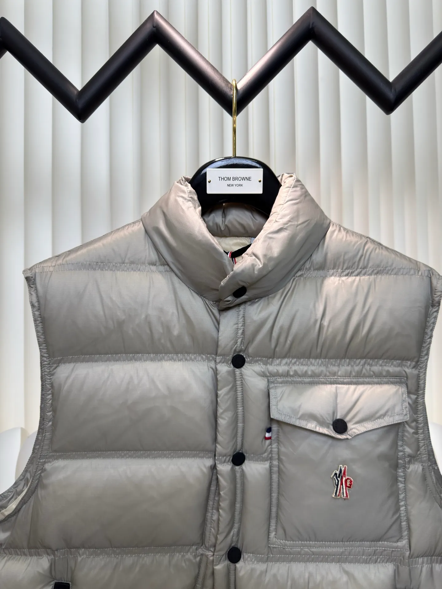 P700 MONCLER masked down vest with reflective markings is made of 90 white duck down with a weight of 130g to ensure excellent thermal insulation performance. After strict screening and processing, the velvet is not easy to get drilled, ensuring durability.  It is made of extremely fine nylon yarn and is woven in a high-density manner. The number of yarns per unit area is large, and the gaps between the yarns are very small, which can effectively block the penetration of cold wind. The fine weave keeps it lightweight and soft to the touch, physically restricting the lightweight down fibers from slipping through the gaps. Nylon fiber itself has good wear resistance and is not easy to snag, which significantly extends its service life and can easily cope with the needs of multiple scenarios.  The lining is made of high-density weaving of 100% polyester fiber, with a thickness of 0.08mm to avoid increasing the overall weight and making it smooth to wear. The high-density weaving structure forms a wind resistance layer to protect the thermal efficiency of the thermal layer from loss. It can withstand the expansion pressure of down and prevent deformation and damage after long-term use.  Through the reflective cloth punching process, the logo is regularly arranged on the triangular reflective mark with dozens of small holes, which not only improves functionality but also enhances recognition and aesthetics. Size 1 2 3 4