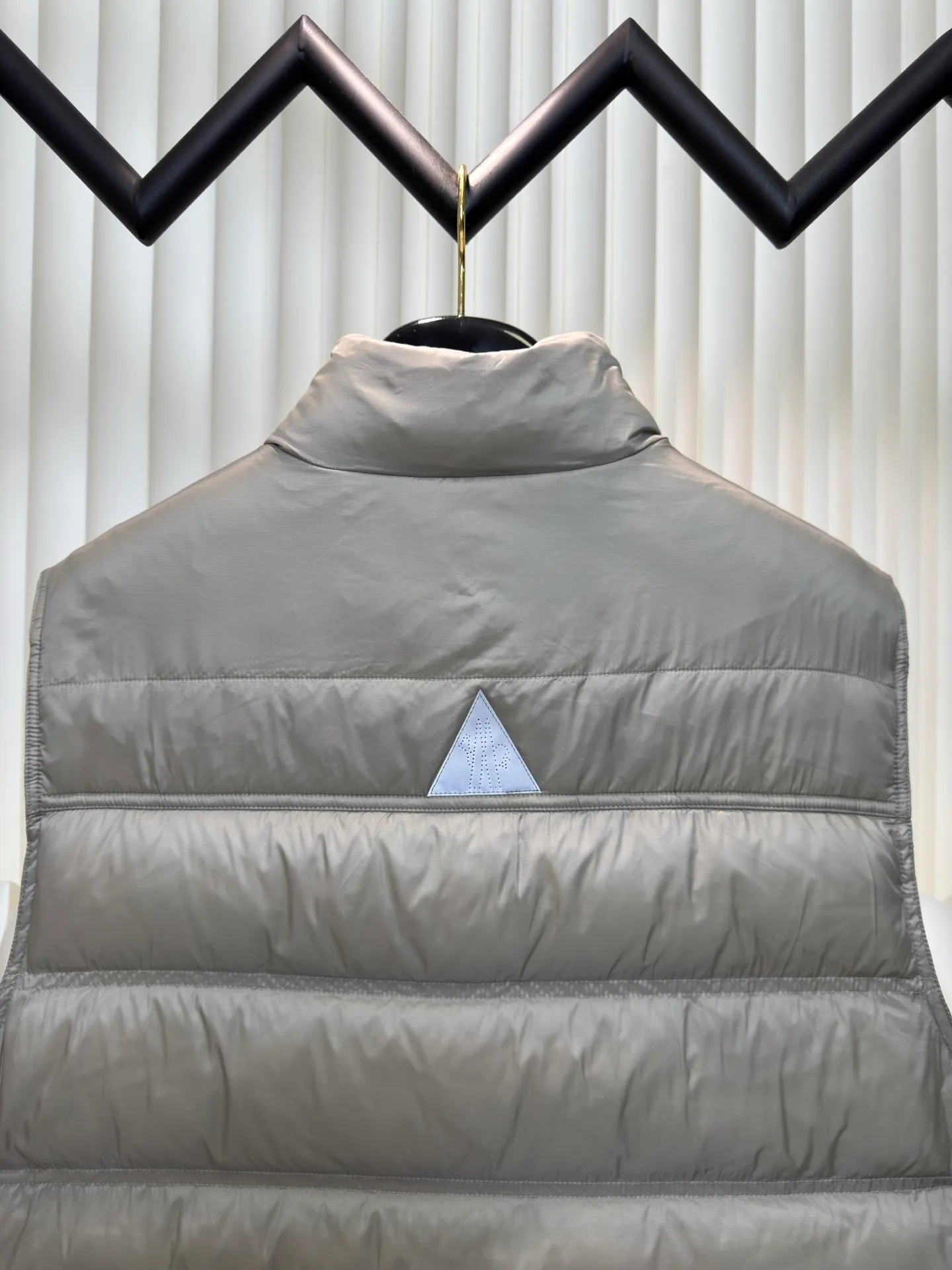 P700 MONCLER masked down vest with reflective markings is made of 90 white duck down with a weight of 130g to ensure excellent thermal insulation performance. After strict screening and processing, the velvet is not easy to get drilled, ensuring durability.  It is made of extremely fine nylon yarn and is woven in a high-density manner. The number of yarns per unit area is large, and the gaps between the yarns are very small, which can effectively block the penetration of cold wind. The fine weave keeps it lightweight and soft to the touch, physically restricting the lightweight down fibers from slipping through the gaps. Nylon fiber itself has good wear resistance and is not easy to snag, which significantly extends its service life and can easily cope with the needs of multiple scenarios.  The lining is made of high-density weaving of 100% polyester fiber, with a thickness of 0.08mm to avoid increasing the overall weight and making it smooth to wear. The high-density weaving structure forms a wind resistance layer to protect the thermal efficiency of the thermal layer from loss. It can withstand the expansion pressure of down and prevent deformation and damage after long-term use.  Through the reflective cloth punching process, the logo is regularly arranged on the triangular reflective mark with dozens of small holes, which not only improves functionality but also enhances recognition and aesthetics. Size 1 2 3 4