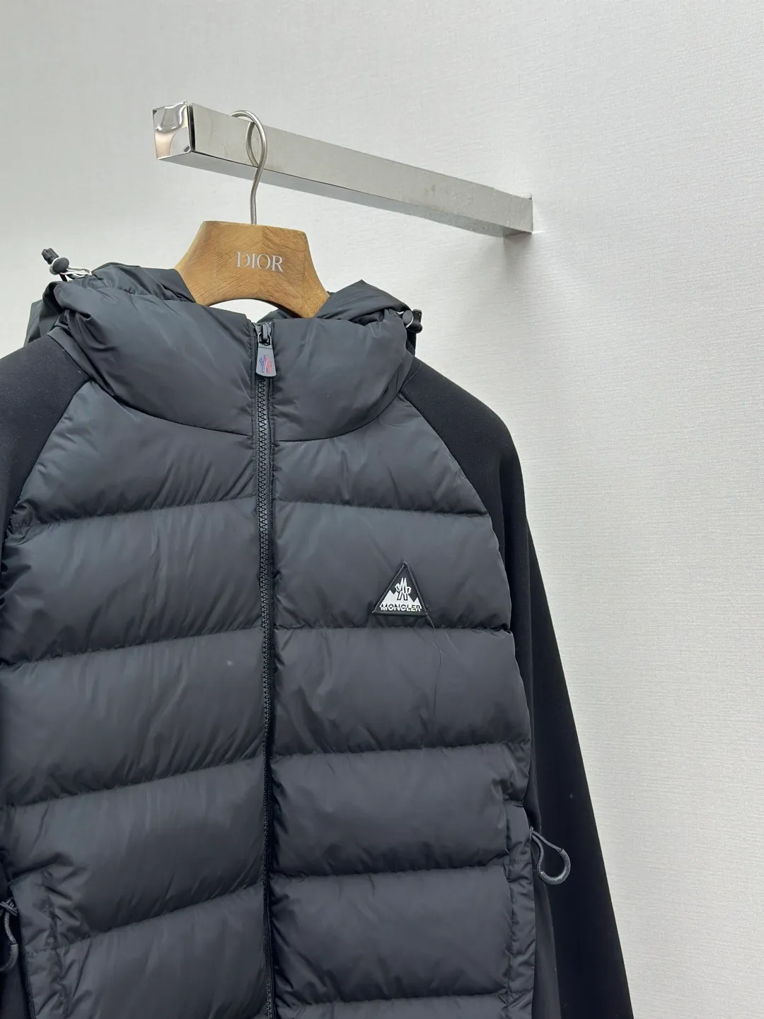 P810 Moncler logo woven splicing down jacket, customized matte crystal lattice air shield velvet and 300D high-density calendered coating, using the new national standard 90 white duck down (welcome to test), full of down, full of warmth, light and fluffy, with the dark green of the overlapping mountains as the background color, all things accumulating, creating its own scenery in silence The Monlcer triangle logo is embellished on the chest, the power aesthetics of the minimalist logo The concentrated down filling in the front area creates dynamic insulation for the core heat dissipation zone of the human body. The hooded down is a moving warm flow barrier for the head and neck, forming a thermal energy circulation system with the front area. The elastic woven sleeves provide freedom of movement with a sense of compression, forming a relaxed and warm philosophy. The real high-end is to let function become the footnote of style. Process 1: Computer mechanical down filling. Prioritize the liner pattern by making a pattern to determine the down filling area and determine the weight of down per square meter according to the original three-dimensional effect. Thus, the amount of down filling for each cut piece is calculated. The computer down filling machine uses a digital weighing unit to achieve stable measurement. Process 2: 3D three-dimensional quilting technology. With the programming system of the CNC quilting machine, the down in different areas is accurately separated to ensure that the filling is evenly fixed after sewing and avoid agglomeration or displacement. Process 3: Computer template machine line running process. The computer template machine line line process shows extremely high neatness and smoothness. The craftsman's precise control of the size during the operation ensures that each line meets the design requirements. The lines of the entire template are smooth and unified, neat and beautiful. Process 4: Triple locking five-thread dense stitching process. Main seam locking + diagonal reinforcement + raw edge wrapping. Triple structure. Forming a three-dimensional protective net at the edge of the fabric to avoid stitch breakage. Paving materials: Customized Moncler zippers. Customized Moncler rope loops. Customized Moncler logo. Customized Moncler eyelets. Customized Moncler trademark. Size: S M L XL