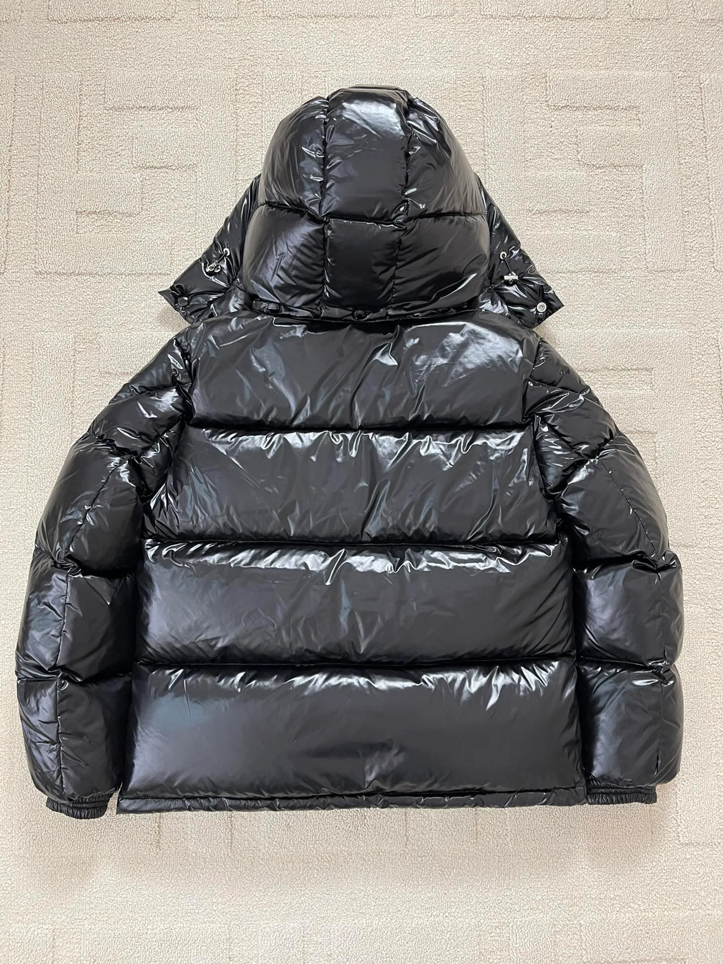 Flat detail P1180 Moncler Montbeliard glossy down jacket The Montbeliard down jacket is made of shiny patented nylon and features highly recognizable rectangular quilting. Featuring a hooded design and signature patch pocket at chest.  Fabric: 100% nylon Filling content: 90% white goose down 250-300g Craftsmanship: Made of nylon laqué fabric Nylon laque lining Filled with down, detachable and adjustable hood with drawstring closure Built-in flap with webbing, black pocket details at the lower end Zipper closure Collar with snap buttons Zipper pockets Patch pockets with snap buttons Adjustable cuffs Adjustable elastic drawstring hem.  Size: 1 2 3 4 5 0548000