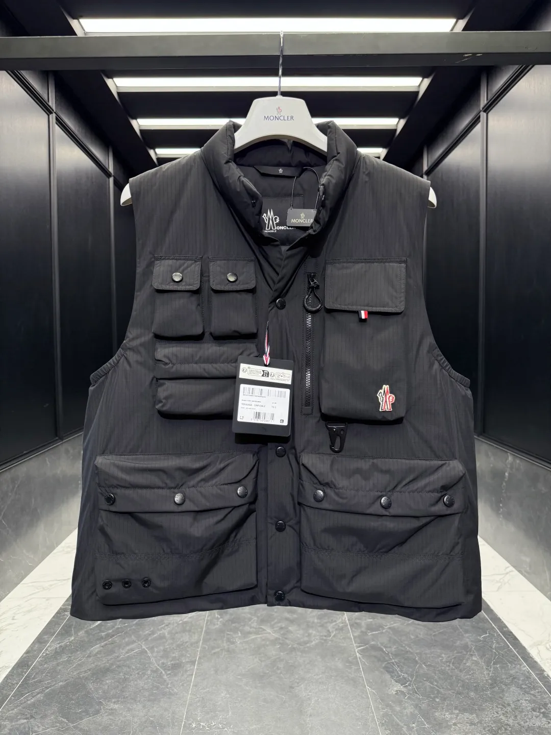 P860 Premium Down⬆️Moncler Grenoble Tongass Down Outdoor Vest. High-end Black Label Series. Original replacement fabric. Premium gooseneck filling. 🎁 Comes standard with a full set of counter gift box packaging. Upgraded original magnetic gift box. The Tongass Down Vest provides protection without being heavy, and is specially designed for outdoor activities in mild weather.  The Tongass down vest is the result of research into lightweight performance outerwear. Functional fabric is tight and durable without adding extra weight. Features a large utility pocket and carabiner clip to reduce the amount of luggage you carry. Details •Designed for outdoor activities •Made from tight fabric •Polyester lining •Down filling •Snap button closure •Utility pockets with snap, zip and Velcro closure •Drawstring hem •Front carabiner •Reflective details Size: 1-5 Cream/Light Brown/Black D00780