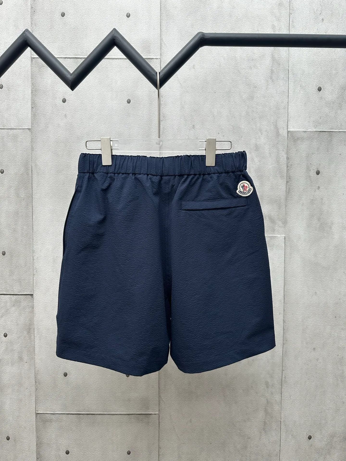 P320 MONCLER Puff Wrinkle Logo Shorts Fabric Selection: Made of cotton blended woven fabric with 76% high cotton content + 24% polyester fiber. The high cotton content ensures that the fabric is soft, skin-friendly, and has good breathability. The addition of a small amount of polyester fiber balances the wrinkle resistance and elasticity of the overall fabric and greatly reduces its shrinkage. After preshrinking, dimensional changes during washing are negligible. The fusion of the two makes the fabric combine anti-wrinkle, quick-drying, easy care and other characteristics without losing the advantages of good wearing experience and strong breathability.  Bubble wrinkle technology: ground warp + bubble warp independent let-off. The bubble warp yarn feeding speed is about 20% higher than the ground warp yarn feeding speed. During weaving, the bubble warp is relaxed and accumulated, forming a naturally arched bubble unit. Through the alternating arrangement of yarns + floating length tissue changes, a clear grid frame is built between the bubble units, and finally the bubble three-dimensional effect and grid outline are locked through high-temperature heat setting.  Accessories: One-to-one customized drawstring head One-to-one customized LOGO labeling SIZE: 1 2 3 4