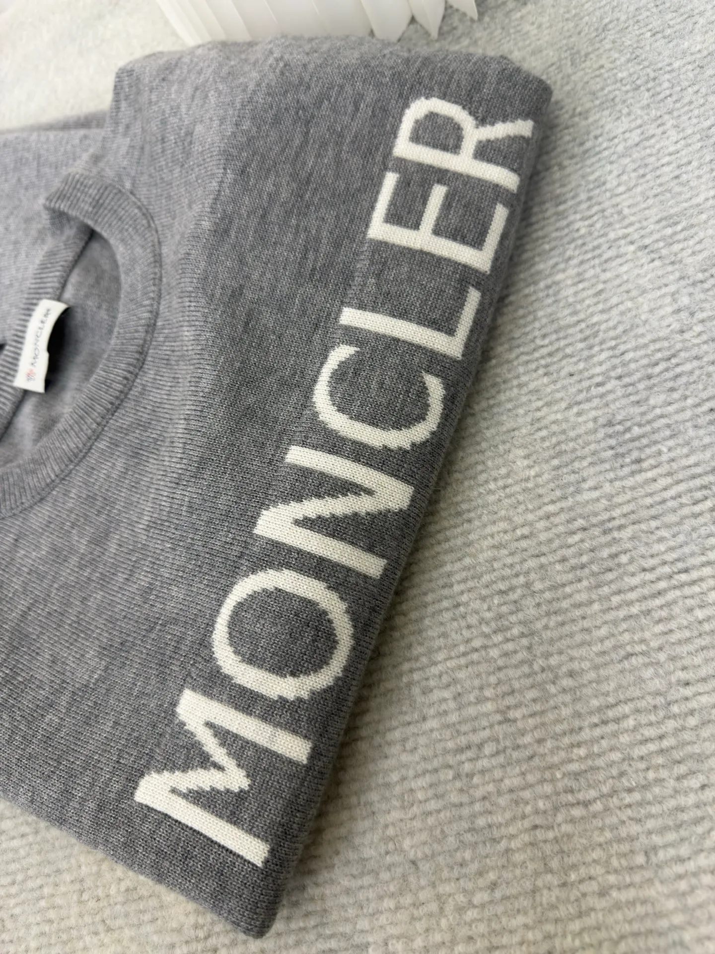 P440 MONCLER jacquard crew neck sweater is made of wool blended fabric, mainly 95% wool, combined with 4% nylon and 1% spandex. The main body of wool ensures the warmth and comfort of the clothing. The addition of a small amount of nylon and spandex significantly improves the elasticity and wear resistance. The ribbed decorative parts are made of 100% wool, which further enhances the overall texture.  Through the high needle count and fine gauge loom, combined with the orderly direction of the internal yarn, the floating threads are cleverly woven and stored, with almost no unnecessary thread mess. The color switching of each group of letters is synchronized with the knitting needles in milliseconds, forming a delicate letter LOGO jacquard decoration on the chest. Size S M L XL