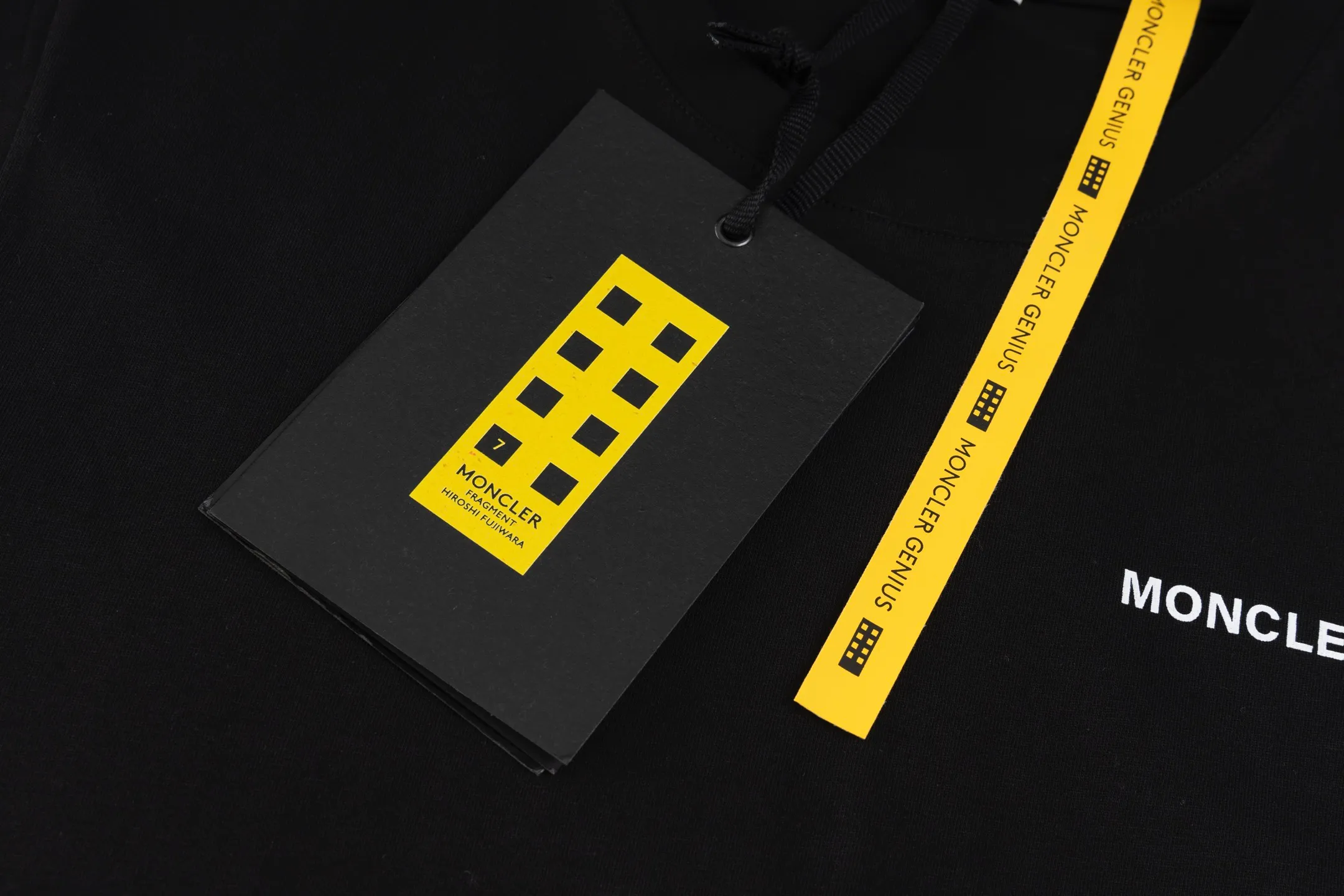 P230 exclusive supply] Moncler Hiroshi Fujiwara co-branded short-sleeve (black) is made of double-ply cotton plain fabric. The warp and weft yarns are interwoven one up and down to form a uniform grid-like texture, with a tight but light structure. Cotton fiber has natural breathability and skin-friendly properties. Combined with the pore structure of plain weave, it is suitable for daily perspiration needs and has good wearing comfort. The yarn has many intertwining points, which strengthens the tear resistance and can maintain its shape after multiple washings. Four high-saturation patterns are presented on the fabric through glue printing. The scraper pressure is even and the scraping is performed in three steps to ensure that the glue is fully penetrated and covered. After curing at high temperature, the pigment is firmly bonded to the cotton fiber. The ink-absorbing and penetrating properties of the cotton fiber make the pattern less likely to fall off due to friction. By actively interfering with the shrinkage potential of cotton fibers, the fabric is able to transition from changeable to stable, improving dimensional stability while being less prone to deformation and wrinkles. Size:S-M-L-XL
