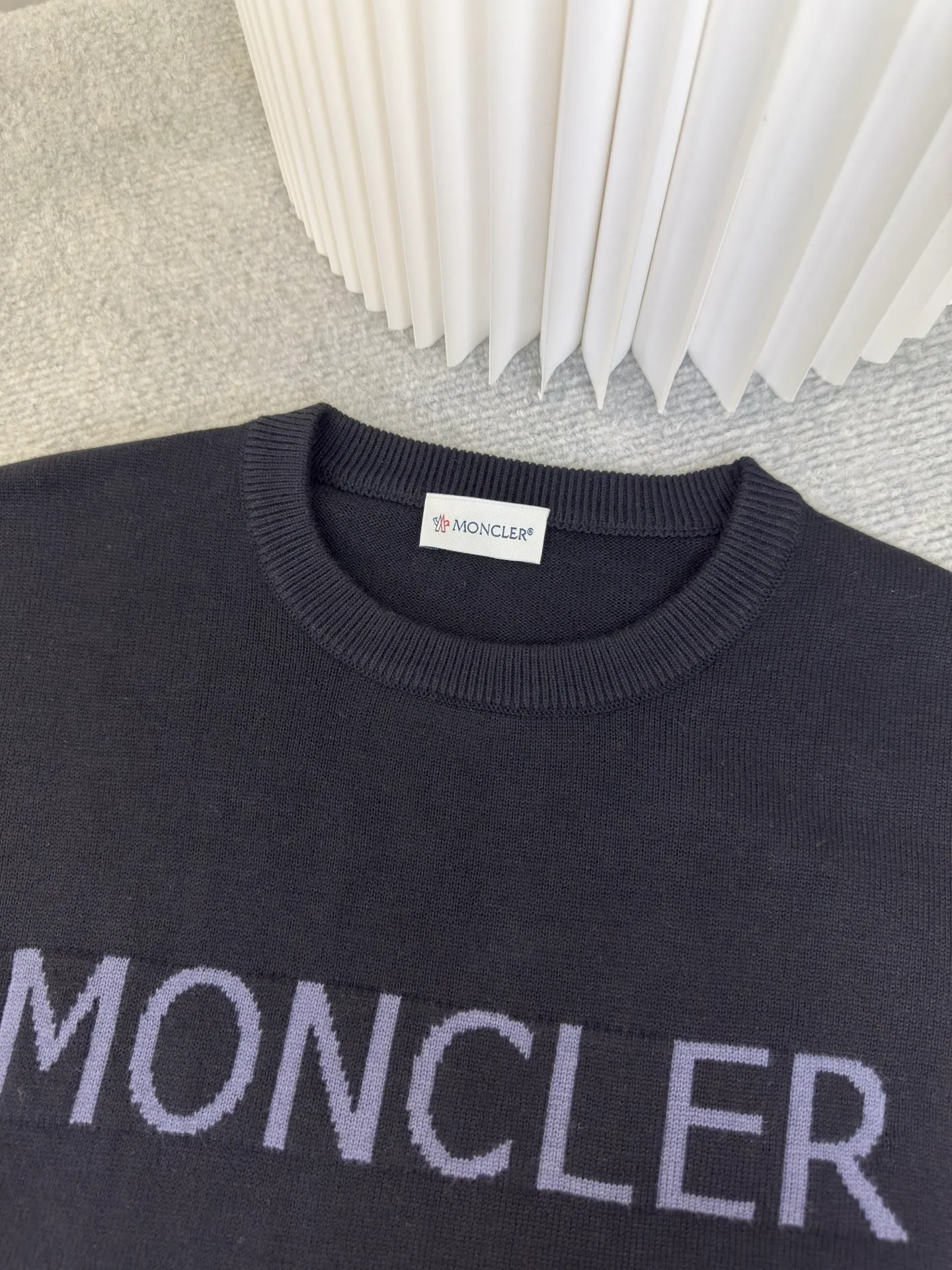 P440 MONCLER jacquard crew neck sweater is made of wool blended fabric, mainly 95% wool, combined with 4% nylon and 1% spandex. The main body of wool ensures the warmth and comfort of the clothing. The addition of a small amount of nylon and spandex significantly improves the elasticity and wear resistance. The ribbed decorative parts are made of 100% wool, which further enhances the overall texture.  Through the high needle count and fine gauge loom, combined with the orderly direction of the internal yarn, the floating threads are cleverly woven and stored, with almost no unnecessary thread mess. The color switching of each group of letters is synchronized with the knitting needles in milliseconds, forming a delicate letter LOGO jacquard decoration on the chest. Size S M L XL