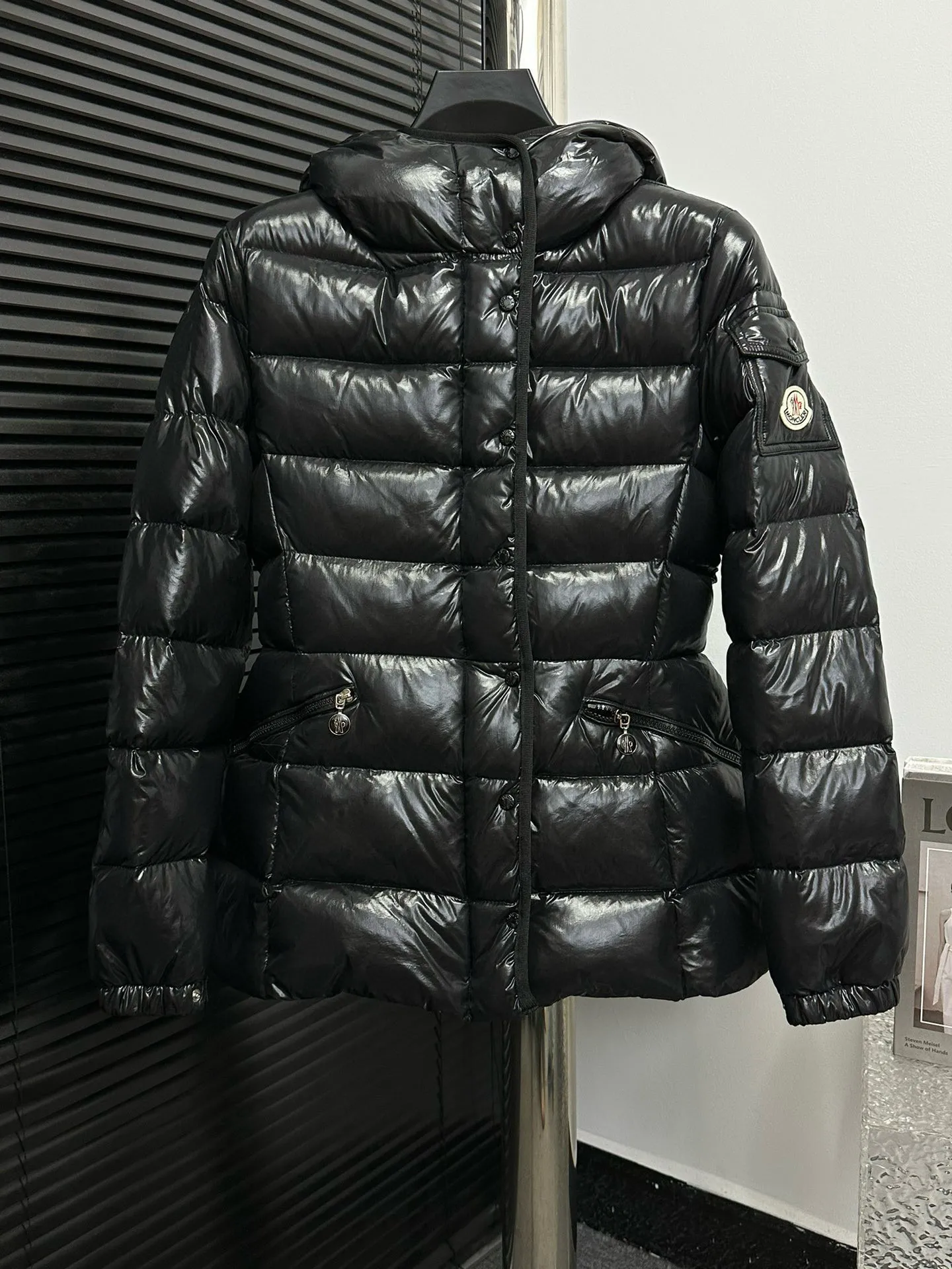 P860 [Moncler] Hooded, waisted women's short down jacket. The barante down jacket is made of glossy nylon fabric and is inspired by the 1970s. It adopts a waist design and presents an A-line silhouette, highlighting a feminine style. An adjustable hood and signature logo patch add finishing touches. Details · Made of lon laqué fabric · lon laqué lining · Filled with down · Adjustable hood · Zipper and snap closure · Suit pocket · Adjustable cuffs Size: 0/1/2/3