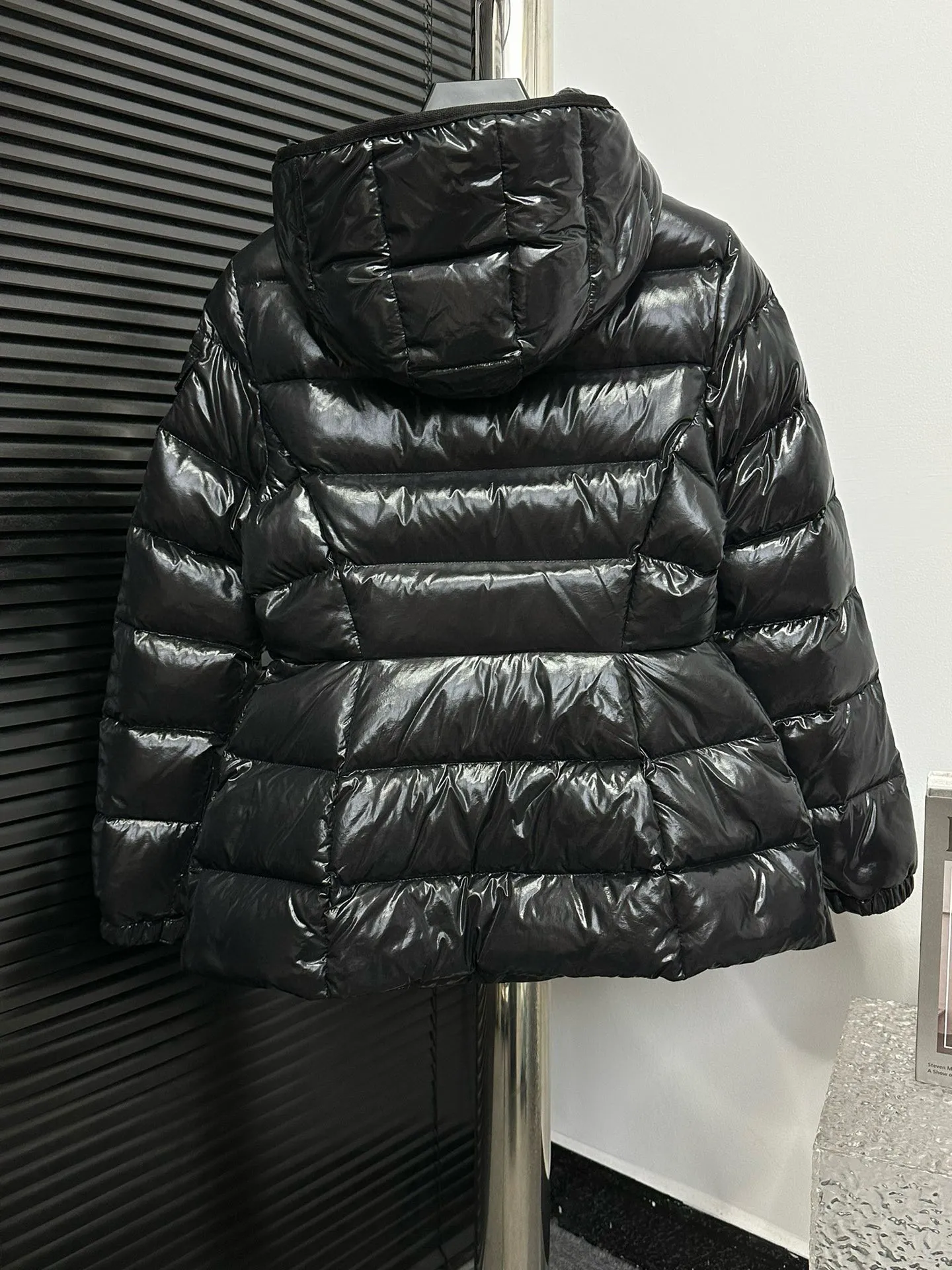 P860 [Moncler] Hooded, waisted women's short down jacket. The barante down jacket is made of glossy nylon fabric and is inspired by the 1970s. It adopts a waist design and presents an A-line silhouette, highlighting a feminine style. An adjustable hood and signature logo patch add finishing touches. Details · Made of lon laqué fabric · lon laqué lining · Filled with down · Adjustable hood · Zipper and snap closure · Suit pocket · Adjustable cuffs Size: 0/1/2/3