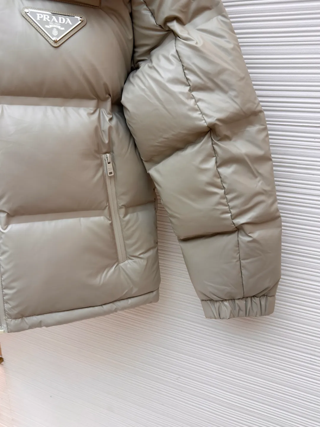 Prada solid color down jacket with removable hood ●Item number: 1682018-D15 ●Fabric: white duck down fabric ●Technology: mechanical down filling ●Color: light khaki gray ●Version: fitted version ●Weight: about 1070 grams ●Size: 48-50-52-54-56 ●Description: This Prada down jacket is made of regenerated nylon fabric, which is treated with high-density weaving and Teflon coating. It is waterproof and wrinkle-resistant and has a matte soft texture. The filling is made of 90% white duck down, and the down is locked in zones through 65-degree diagonal quilting technology. The stitch length is precisely controlled at 3 stitches/cm to avoid down fleece and give the body three-dimensional bulk. The detachable hood is fixed with metal snaps, and the bevel stitching on the neckline improves the fit; the triangle logo on the chest is presented in metal relief, seamlessly connecting with the same-color stitching on the body. The cuffs and hem are equipped with elastic ribs, the side invisible zipper pockets are hot-melt bonded, and the brand's customized hardware accessories are used in every detail, taking into account functionality and luxury texture. The overall wiring is straight and delicate, the fabric is comfortable and soft, and the color is consistent without color difference. It can be matched with the same style to create a fashionable look and control various occasions. Customized accessories, complete with three standards, same style for men and women!