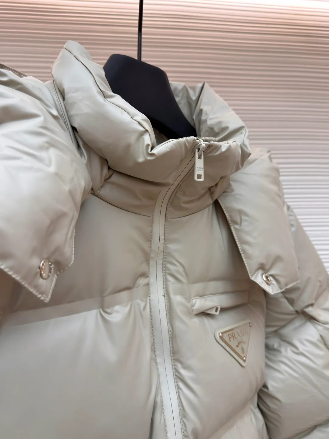 Prada solid color down jacket with removable hood ●Item number: 1682018-D15 ●Fabric: white duck down fabric ●Technology: mechanical down filling ●Color: light khaki gray ●Version: fitted version ●Weight: about 1070 grams ●Size: 48-50-52-54-56 ●Description: This Prada down jacket is made of regenerated nylon fabric, which is treated with high-density weaving and Teflon coating. It is waterproof and wrinkle-resistant and has a matte soft texture. The filling is made of 90% white duck down, and the down is locked in zones through 65-degree diagonal quilting technology. The stitch length is precisely controlled at 3 stitches/cm to avoid down fleece and give the body three-dimensional bulk. The detachable hood is fixed with metal snaps, and the bevel stitching on the neckline improves the fit; the triangle logo on the chest is presented in metal relief, seamlessly connecting with the same-color stitching on the body. The cuffs and hem are equipped with elastic ribs, the side invisible zipper pockets are hot-melt bonded, and the brand's customized hardware accessories are used in every detail, taking into account functionality and luxury texture. The overall wiring is straight and delicate, the fabric is comfortable and soft, and the color is consistent without color difference. It can be matched with the same style to create a fashionable look and control various occasions. Customized accessories, complete with three standards, same style for men and women!